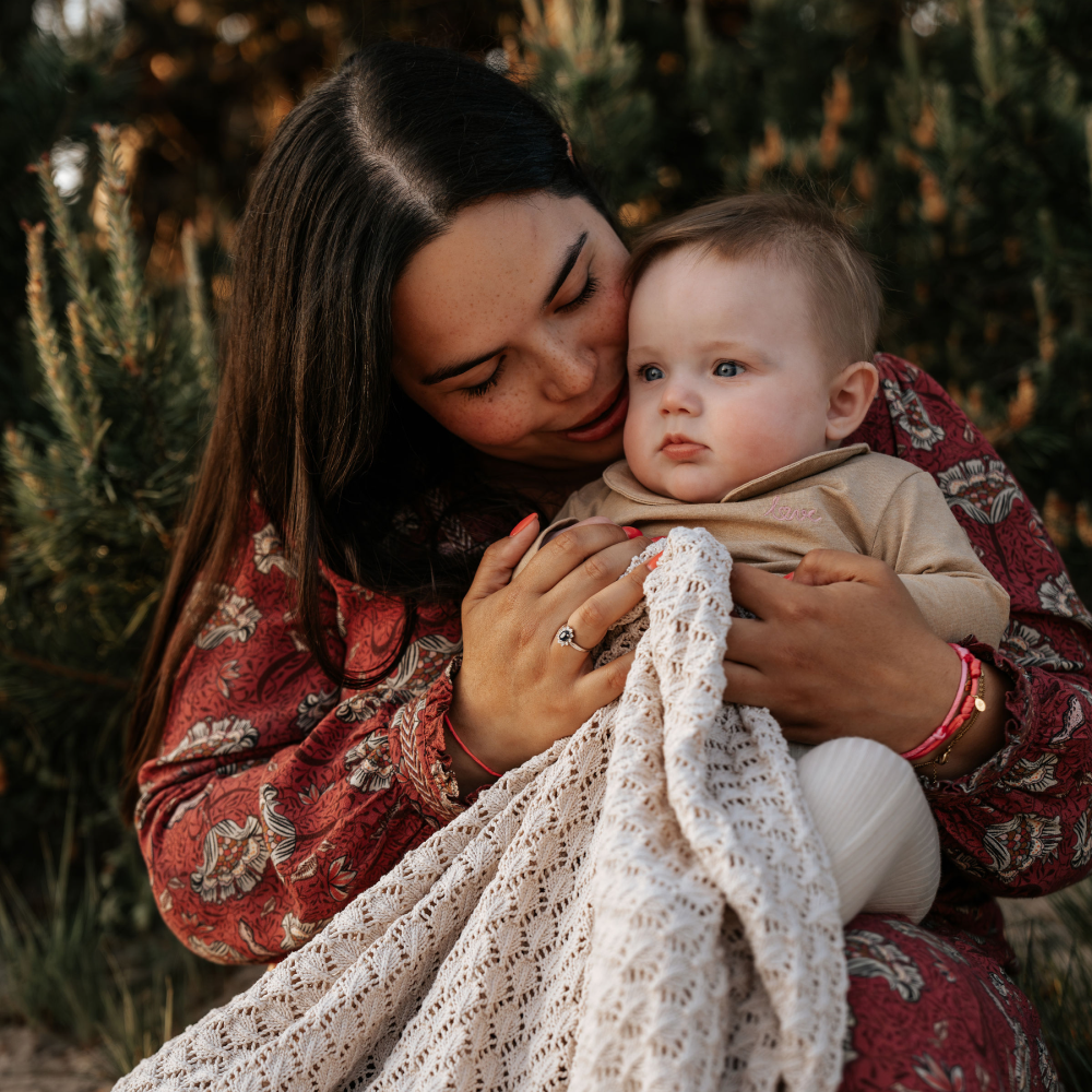 Een vrouw knuffelt een baby in een bos, beiden zien er ontspannen en liefdevol uit tijdens de motherhood shoot.