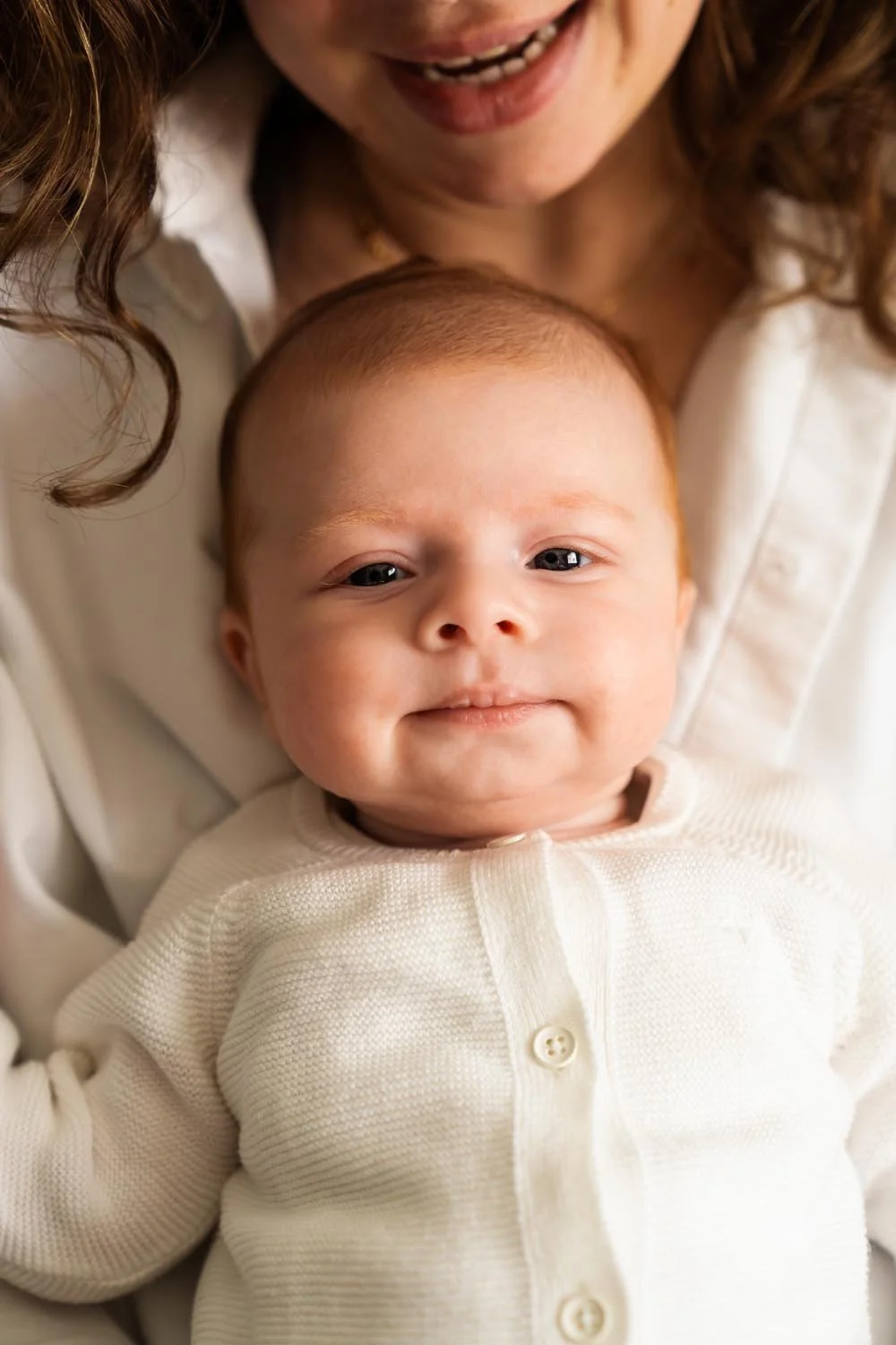 Newborn baby shoot - Baby met rood haar ligt op de schoot van moeder, met bruin haar tijdens de fotoshoot.