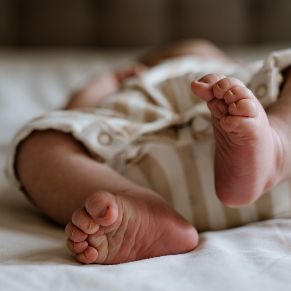 Close-up van baby's voeten op een bed, met een stukje babyromper zichtbaar, van een newborn shoot.