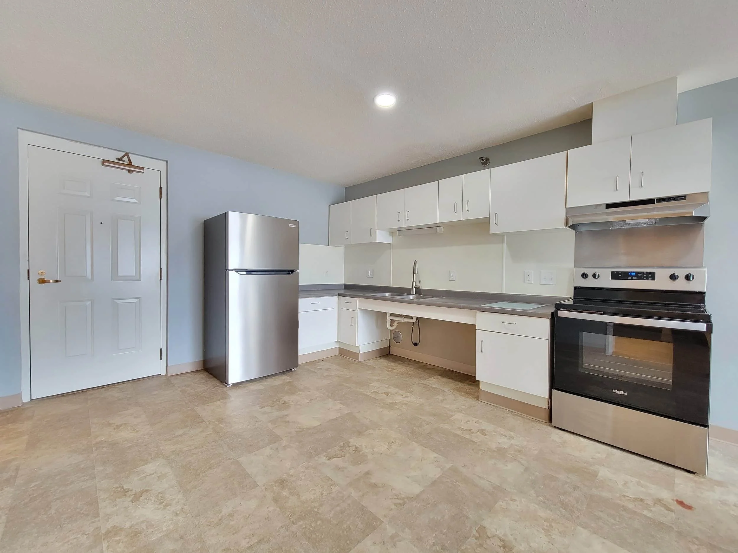 Modern kitchen in apartments in Rochester with white cabinets, stainless steel appliances, beige tile floor, and light blue walls.