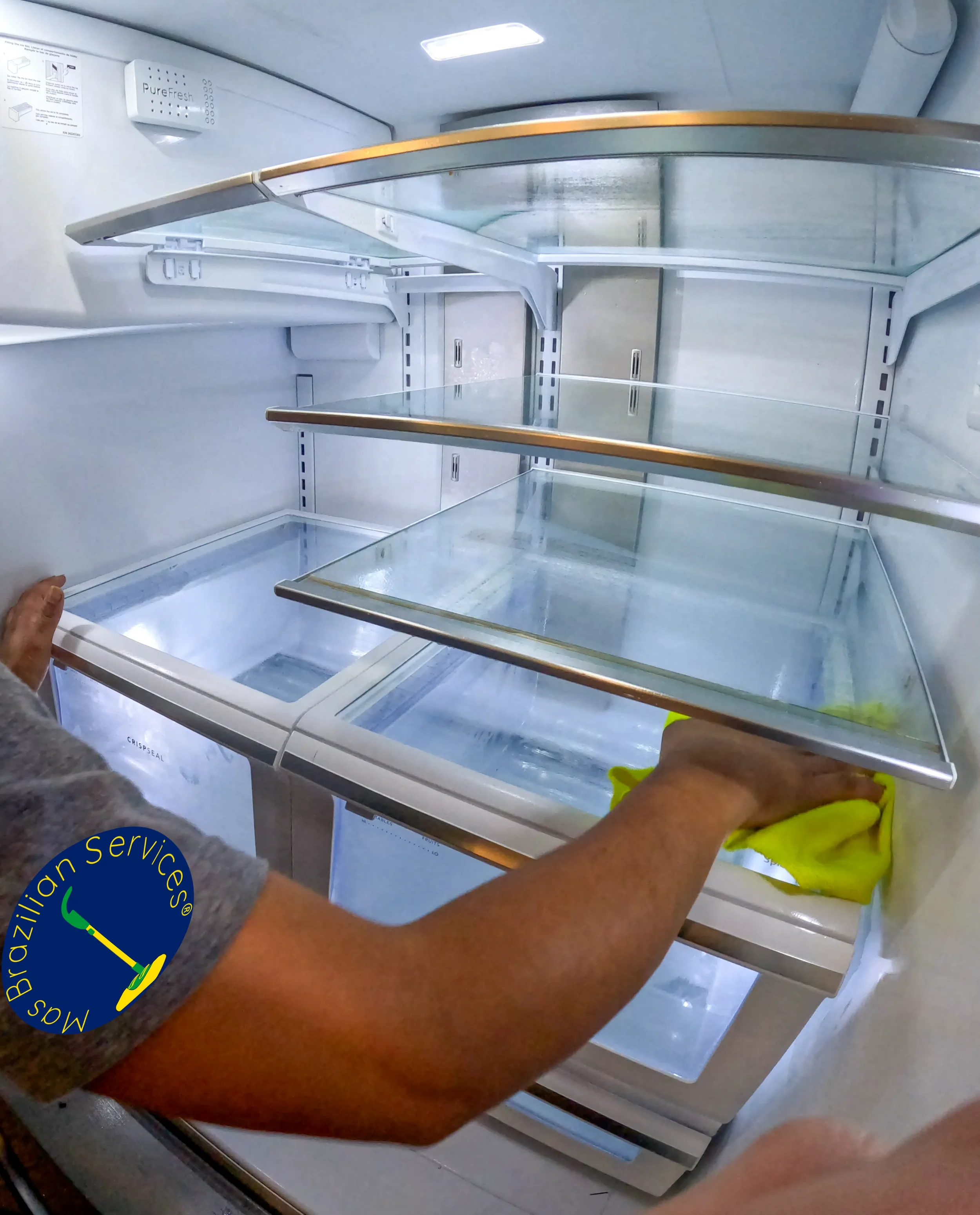 Cleaning professional hand-cleaning and polishing glass shelves and drawers inside a refrigerator, with interior lights illuminating reflective surfaces during deep cleaning.