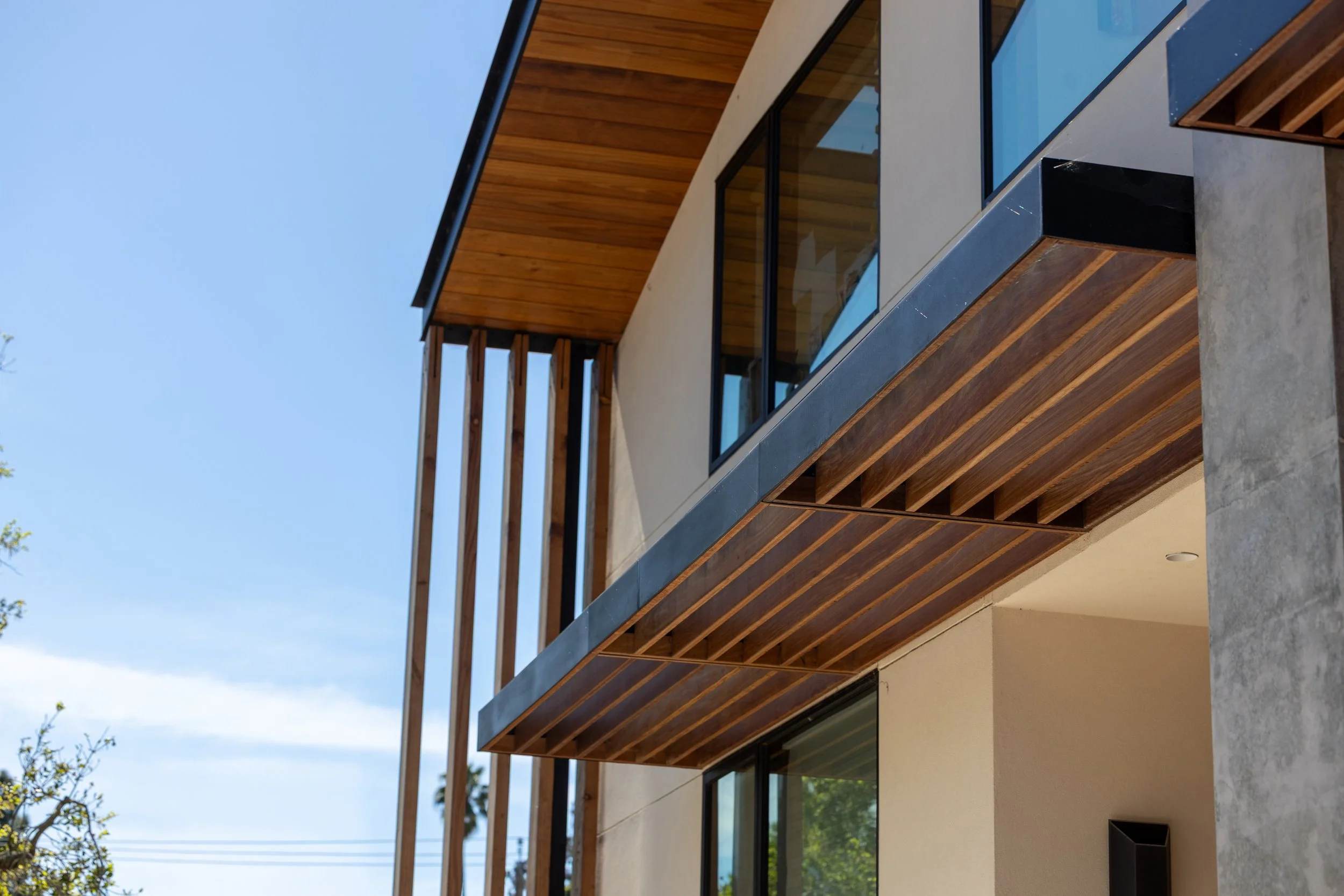 Modern multi-story house with large windows, wooden accents, and a balcony, under a clear Menlo Park blue sky.