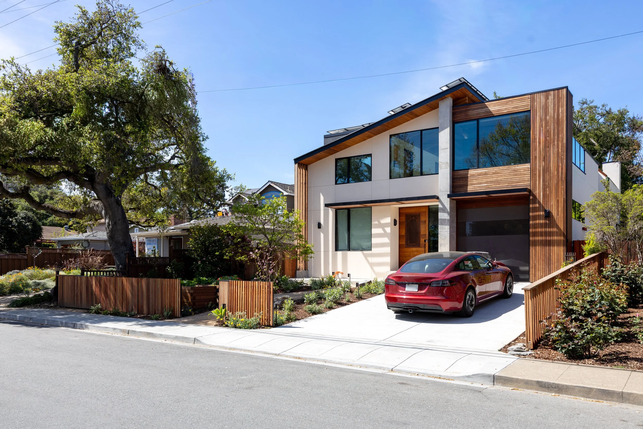 Modern two-story house in Menlo Park, CA with a mix of wood and stucco exterior, large windows, and a red Tesla car parked in the front driveway. 