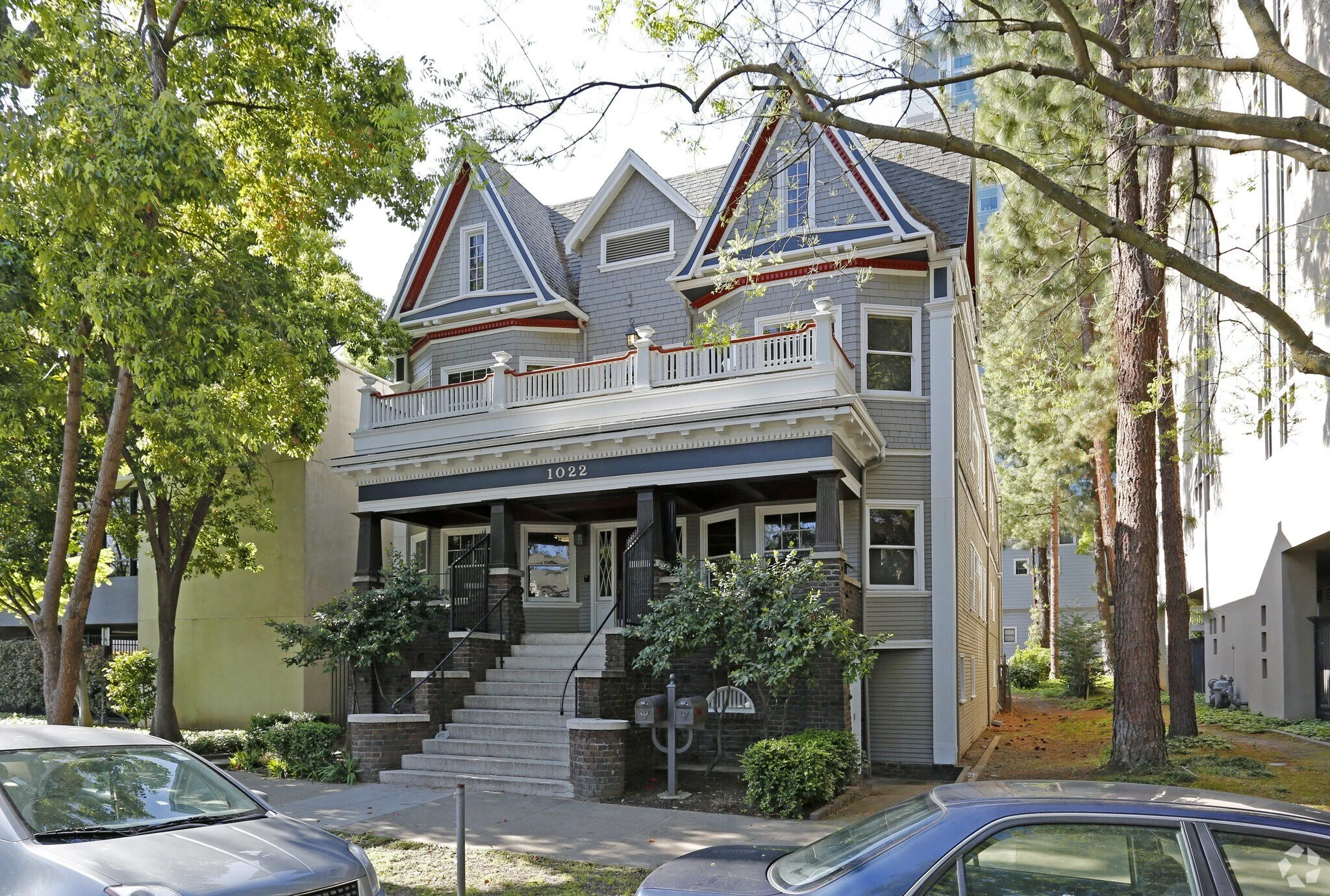 A multi-story Sacramento live/work historic building with a large porch, surrounded by trees and parked cars in the foreground.