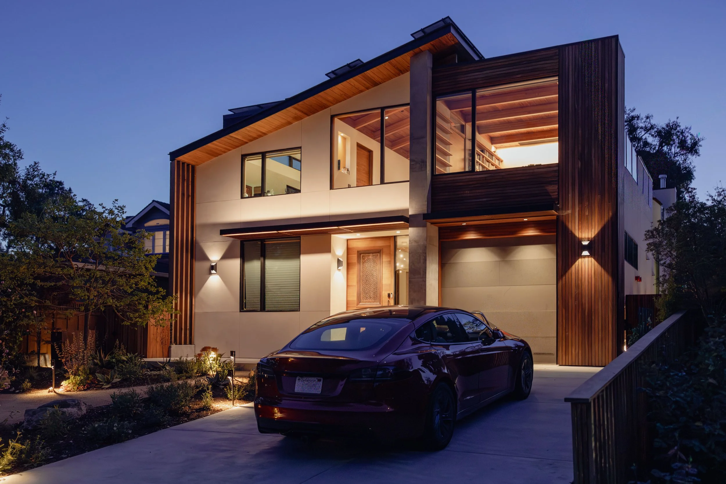 Modern two-story house in Menlo Park, CA with a mix of wood and stucco exterior, large windows, and a red Tesla car parked in the front driveway. 