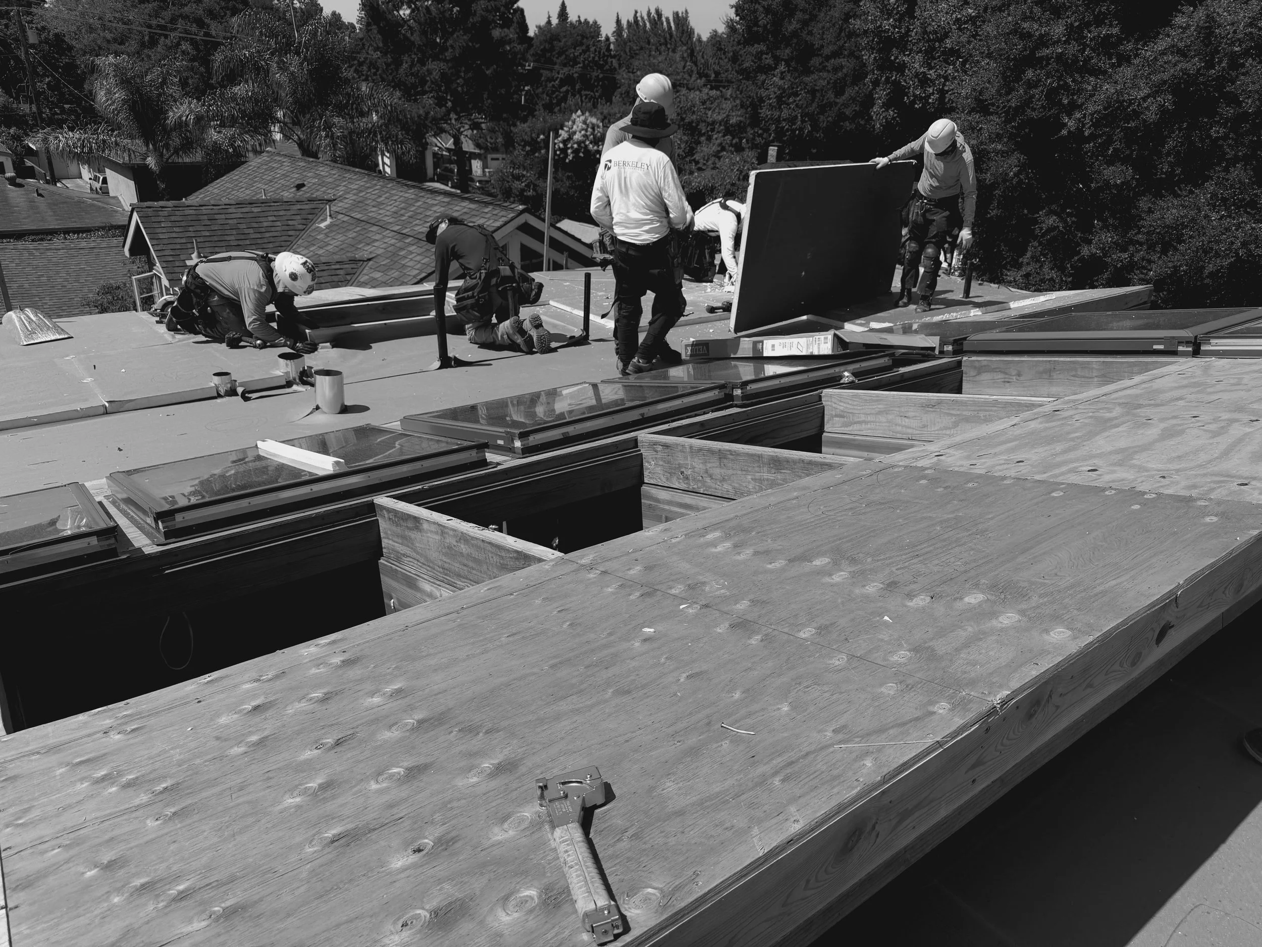 Construction workers on a roof installing solar panels in a California Bay Area home while wearing safety helmets and gloves, with tools and materials around them.