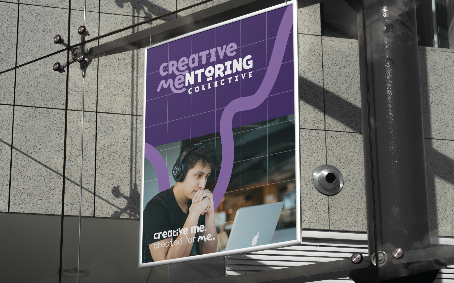 A large outdoor poster advertising the Creative Mentoring Collective, featuring a young man wearing headphones and working on a laptop.