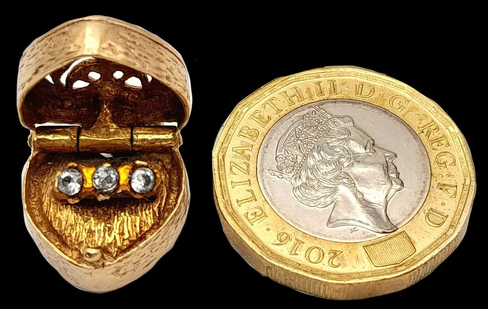 Scale view of gold heart locket beside 1 pound coin
