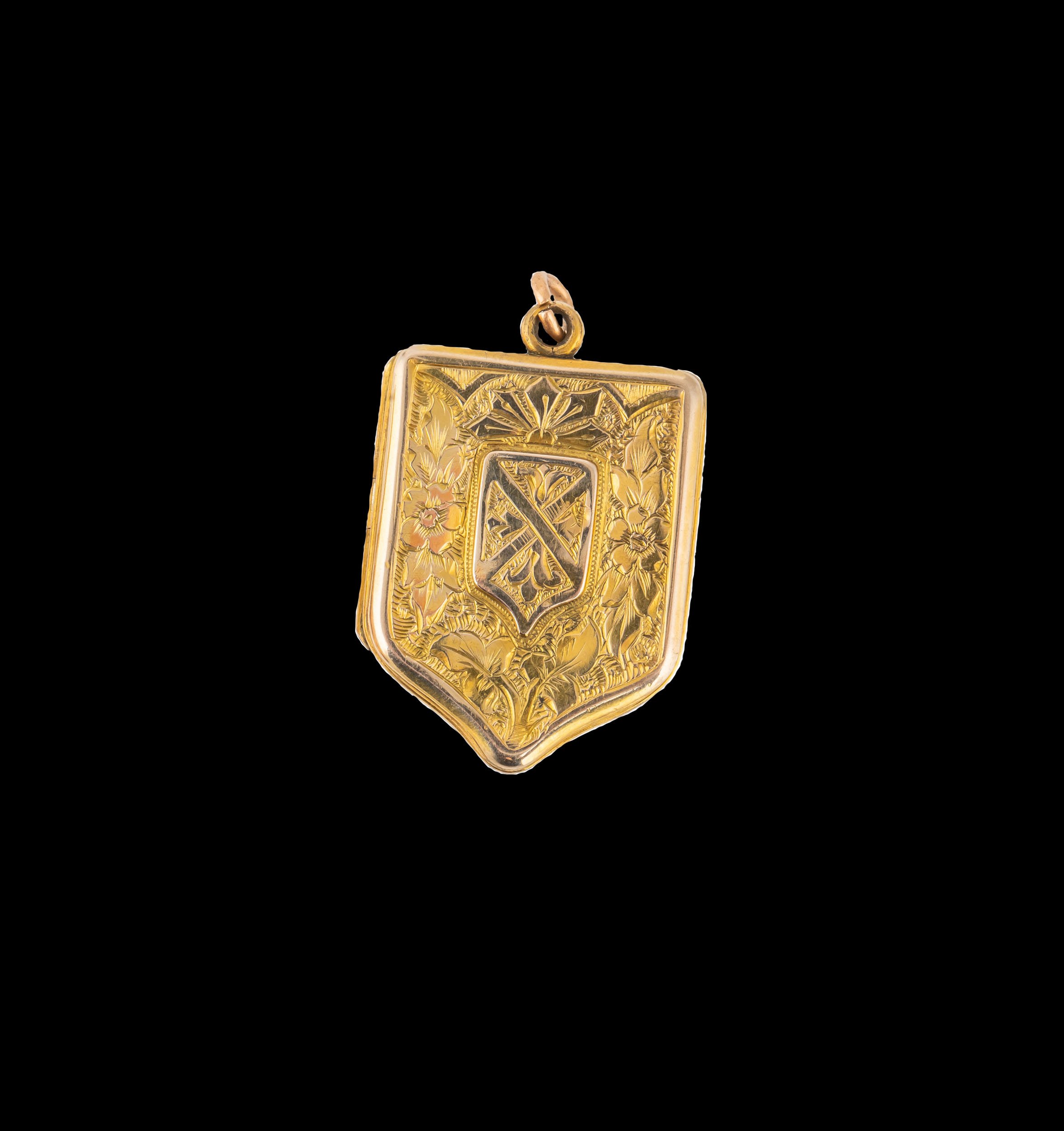 Victorian 9K gold shield-shaped locket with engraved floral and heraldic design on black background