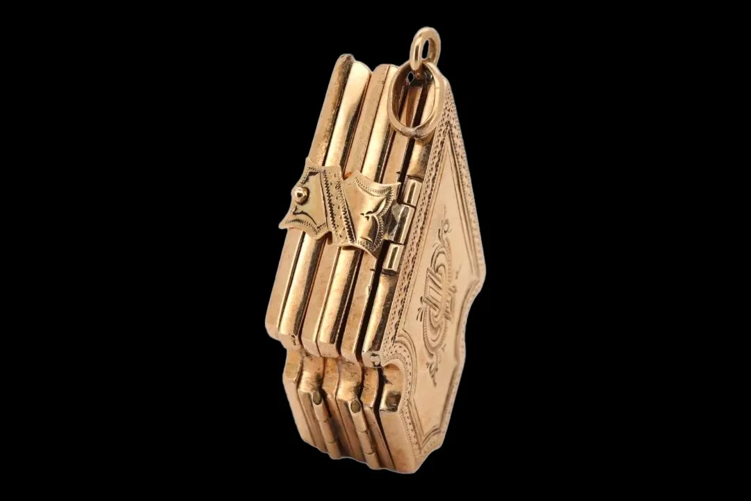 Side view of a Victorian 9ct gold six-compartment folding locket showing layered hinged panels, ornamental clasp, and suspension ring.