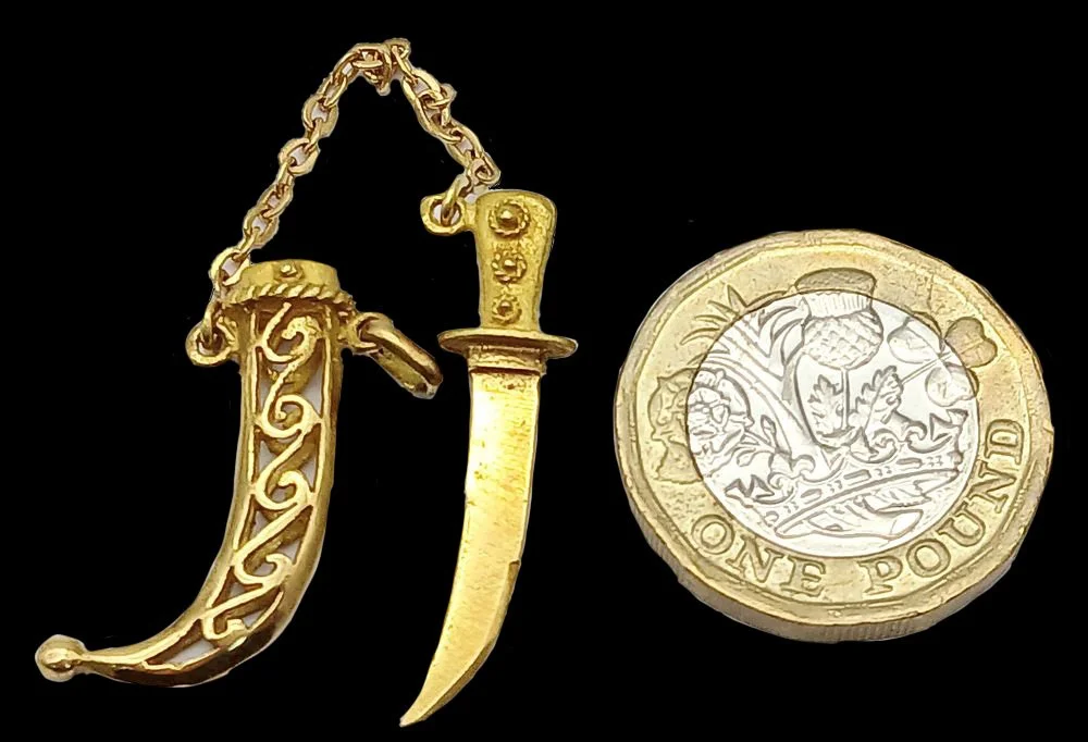 Miniature gold dagger charm shown beside coin