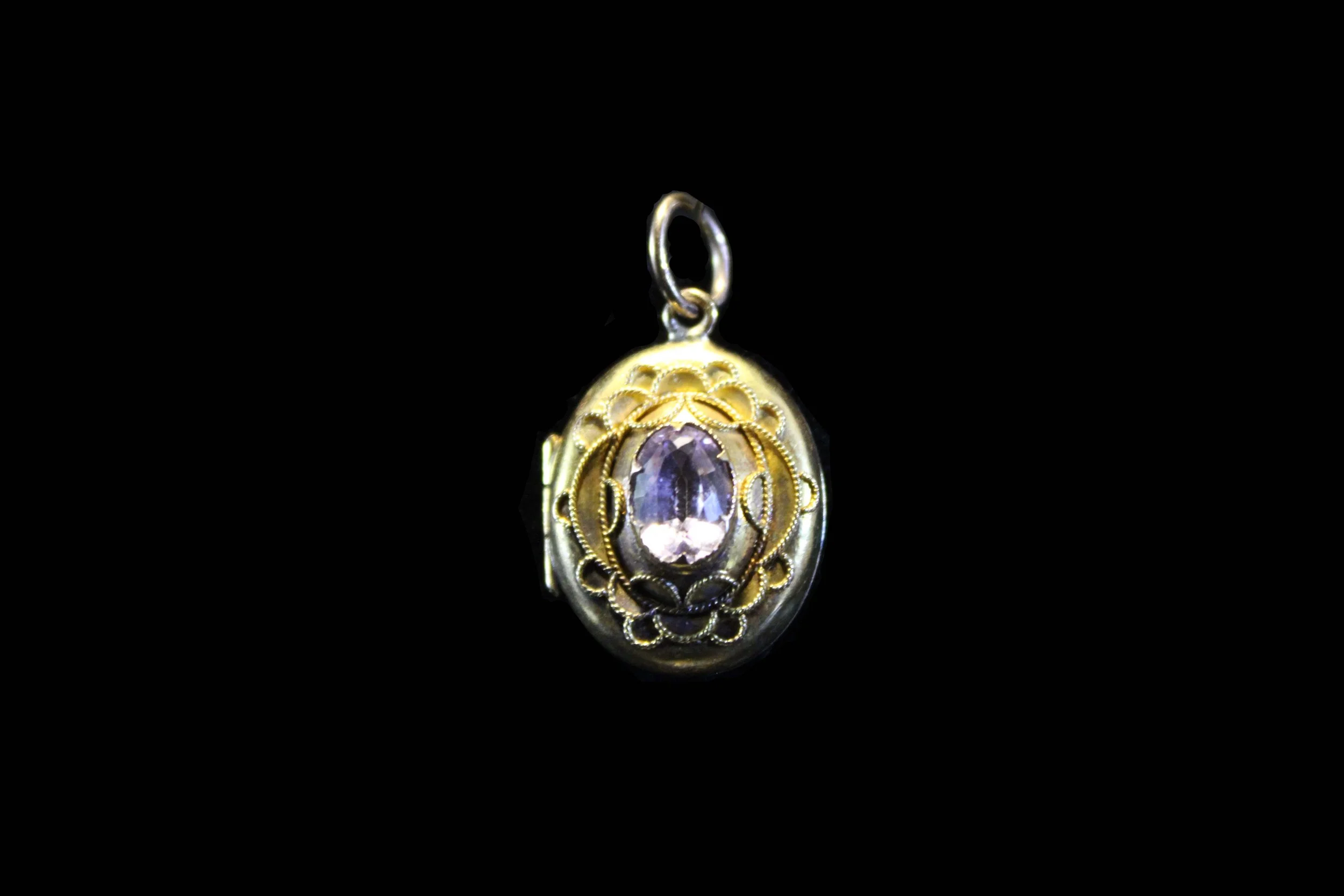 Angled view of Victorian gold oval locket highlighting faceted gemstone and intricate metalwork