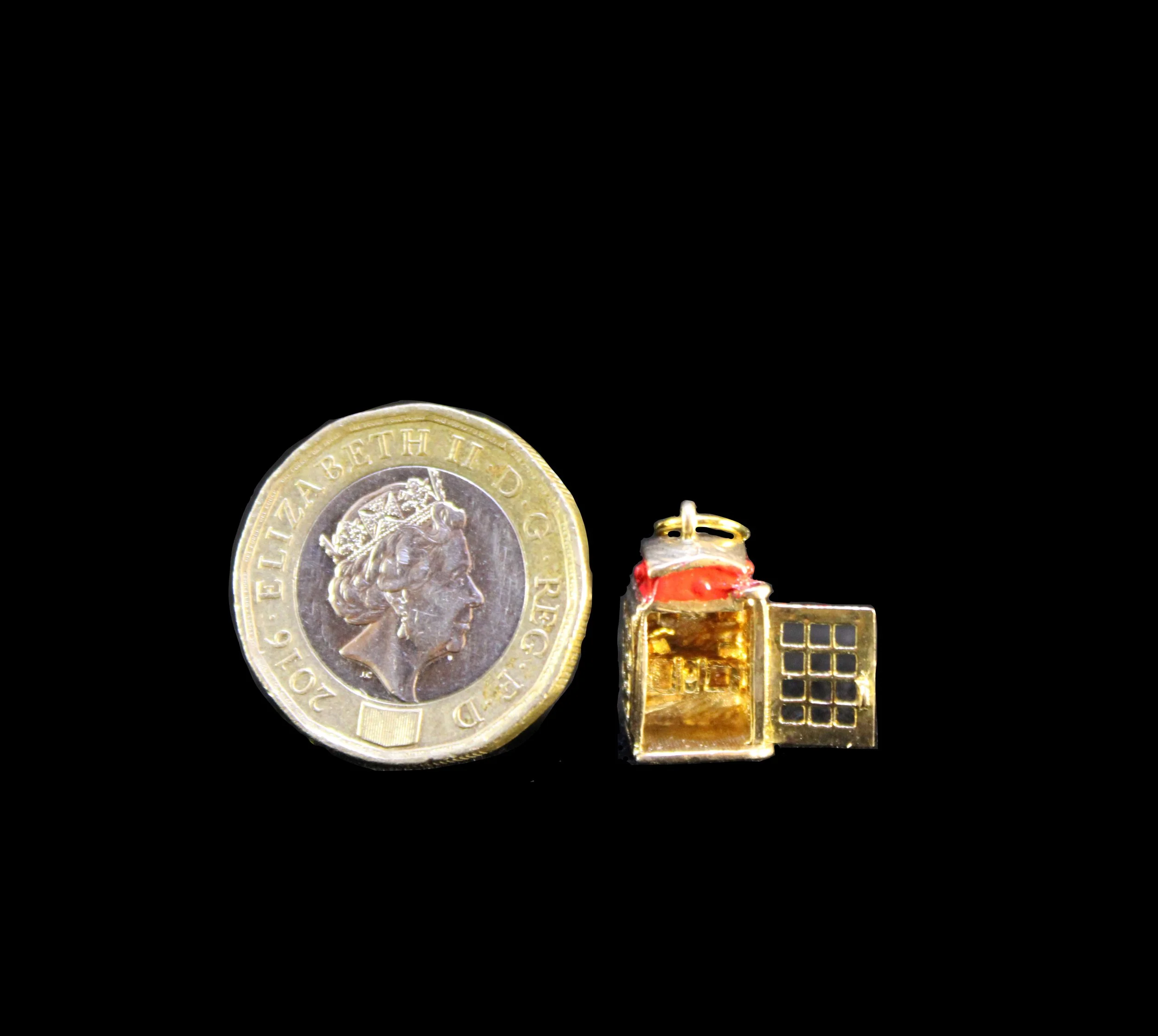 Scale view of gold telephone booth charm beside coin