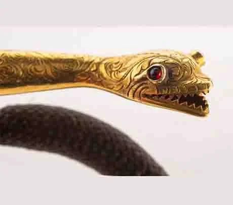 A gold snake with detailed carvings, a red eye, and sharp teeth on hairwork bracelet