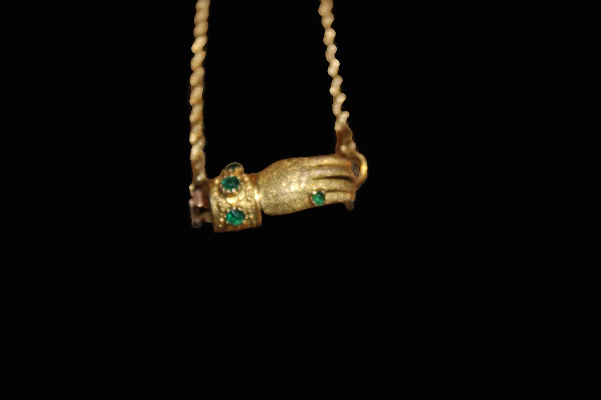 Victorian 9K gold hand clasp bracelet suspended to show sculptural clasp set with green cabochons.