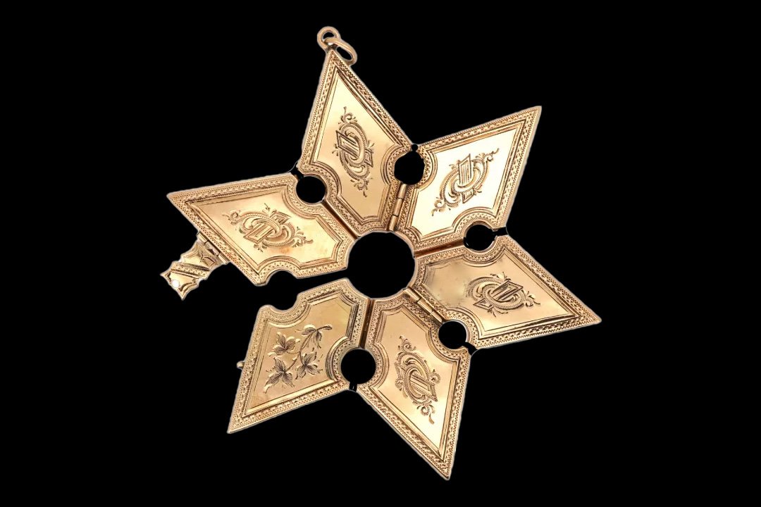 Victorian 9ct gold folding locket opened into a six-pointed star, displaying engraved floral motifs, ornate monograms, and hinged gold panels.