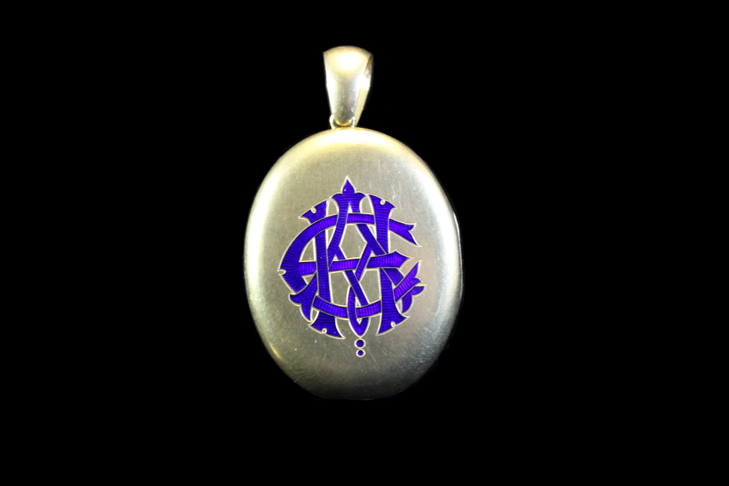 Antique Victorian gold oval locket with cobalt blue enamel monogram in Gothic script, photographed on black background