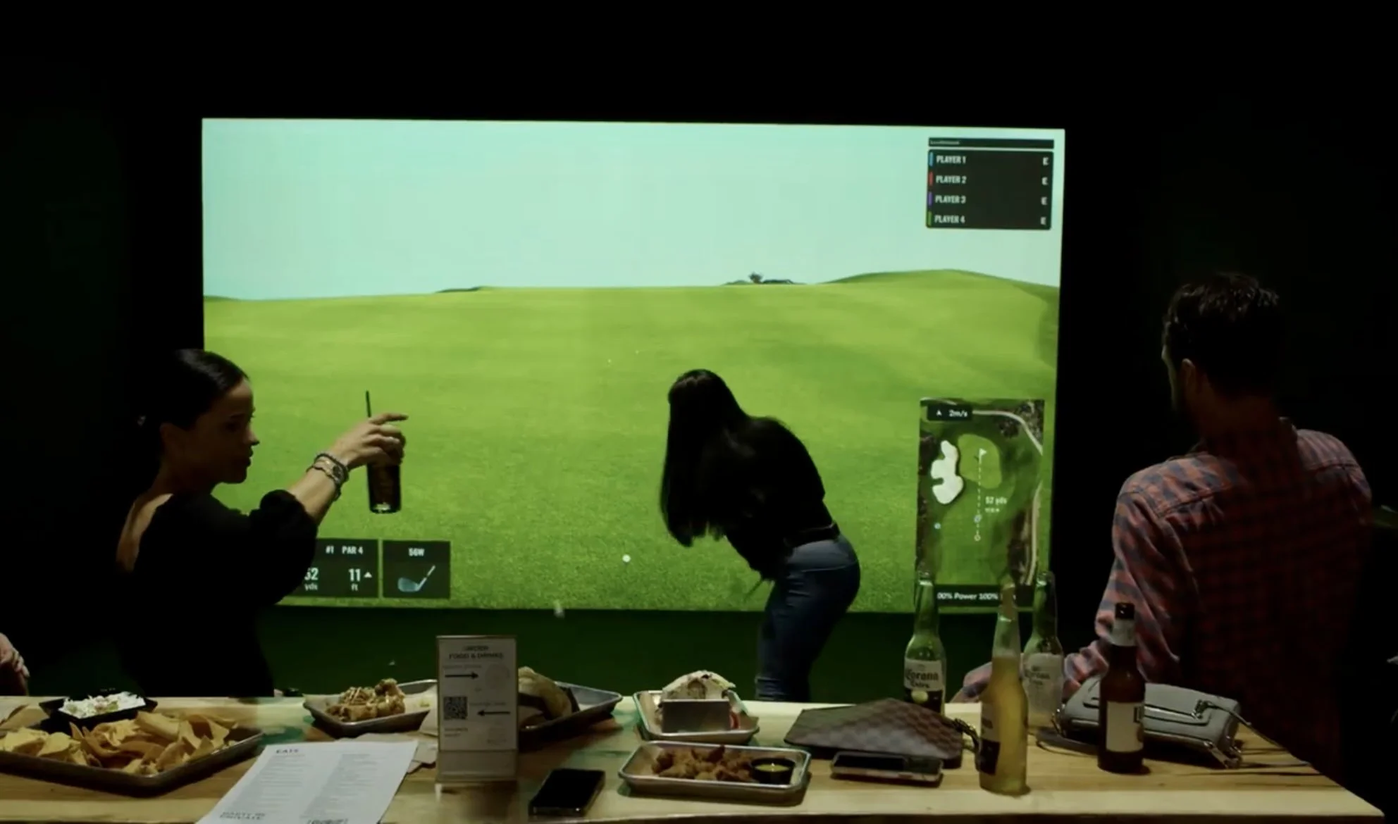 Group of friends enjoying drinks and food while playing a Trackman golf simulator at Back 9 Social in Wallingford, CT