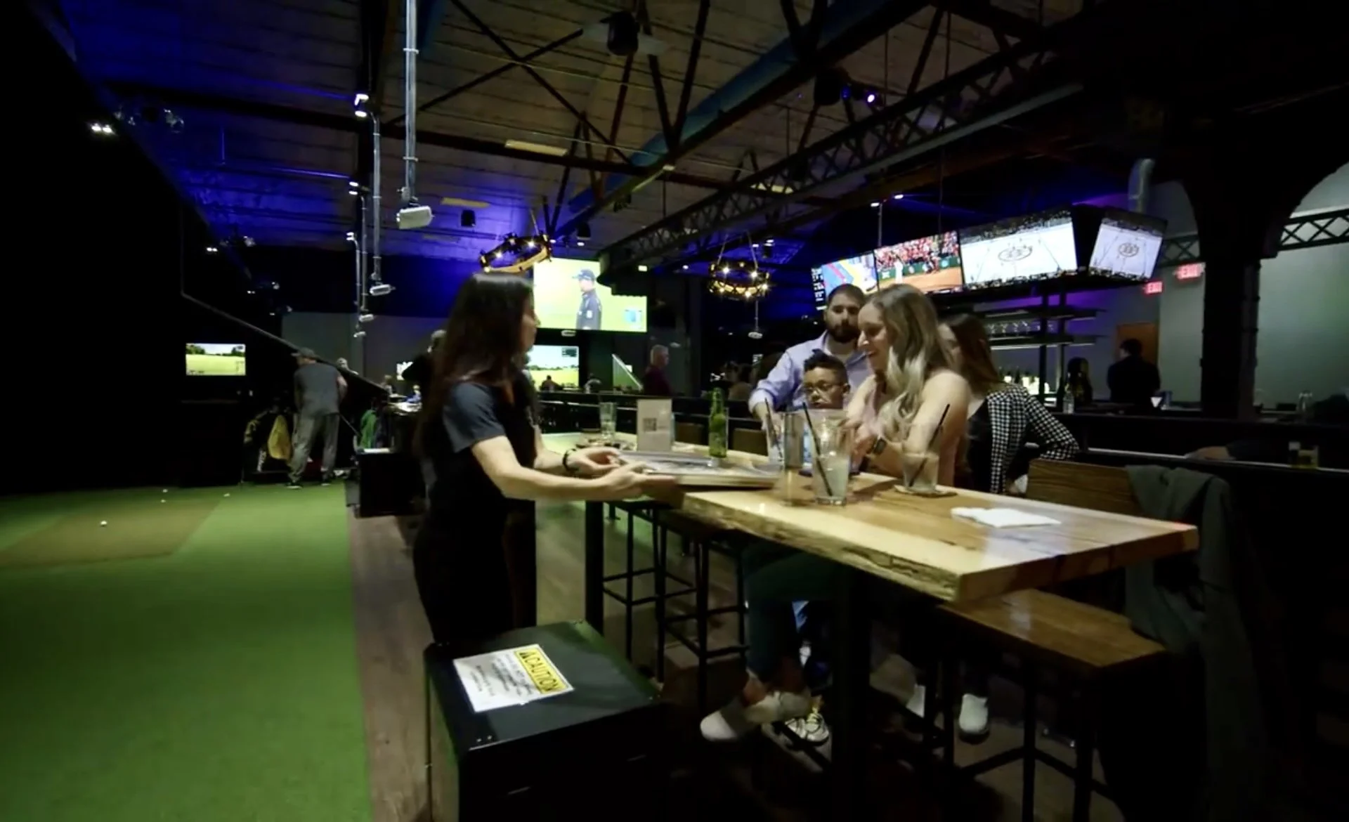 Server taking an order from guests at a table alongside the golf simulator bays at Back 9 Social in Wallingford, CT