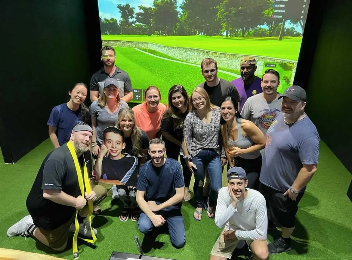 Large group posing for a photo in a Trackman golf simulator bay at Back 9 Social in Wallingford, CT