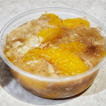 A clear plastic container filled with peach cobbler, showing peach slices, and a crumbly topping.