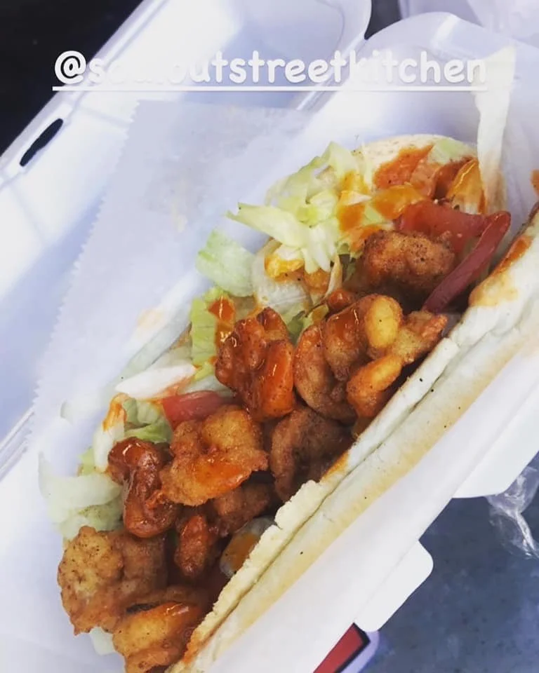 Fried chicken topping a hot dog bun with lettuce and tomato slices in a takeout container.