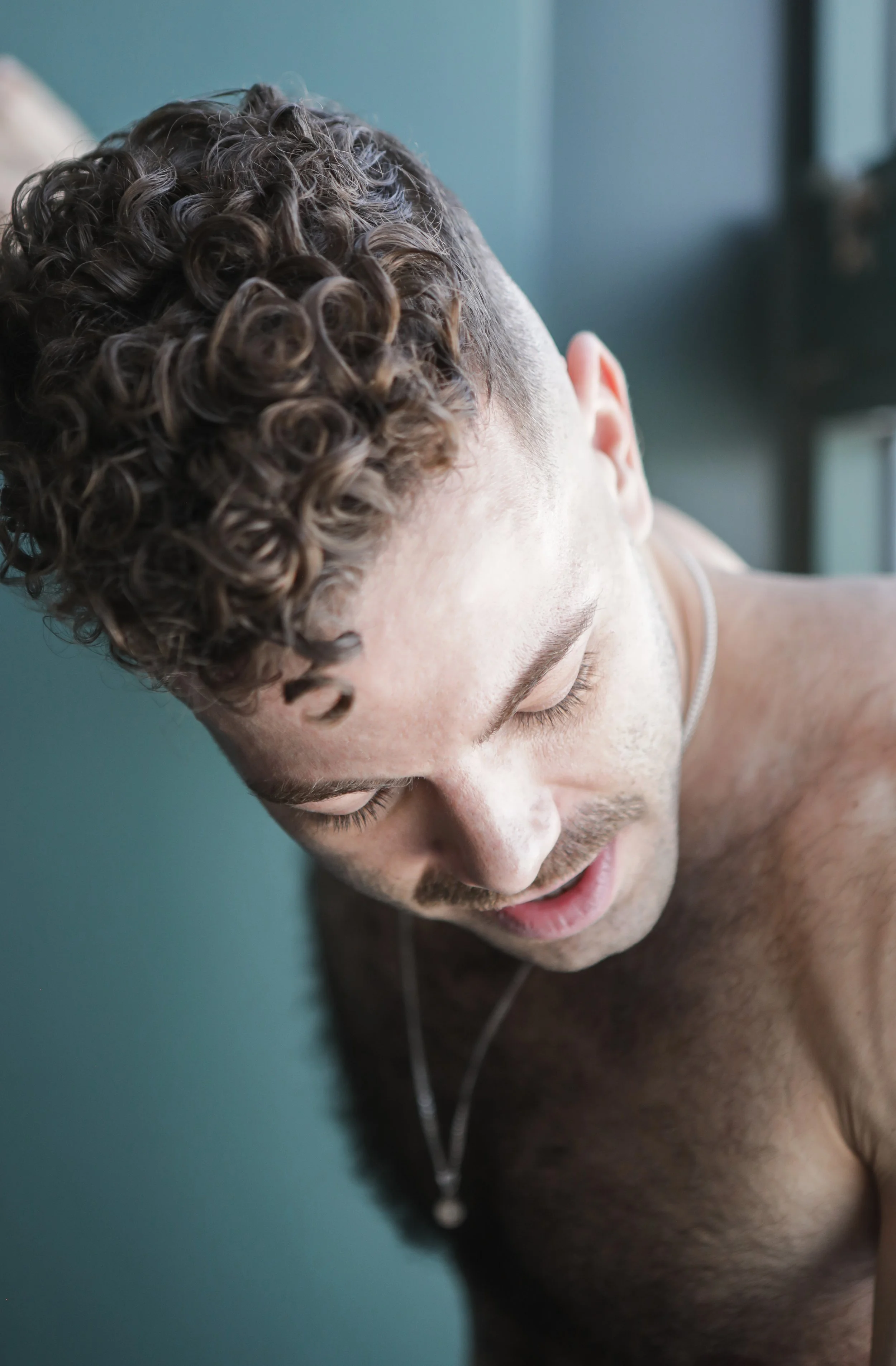Close-up of a shirtless young man with curly hair, looking down.