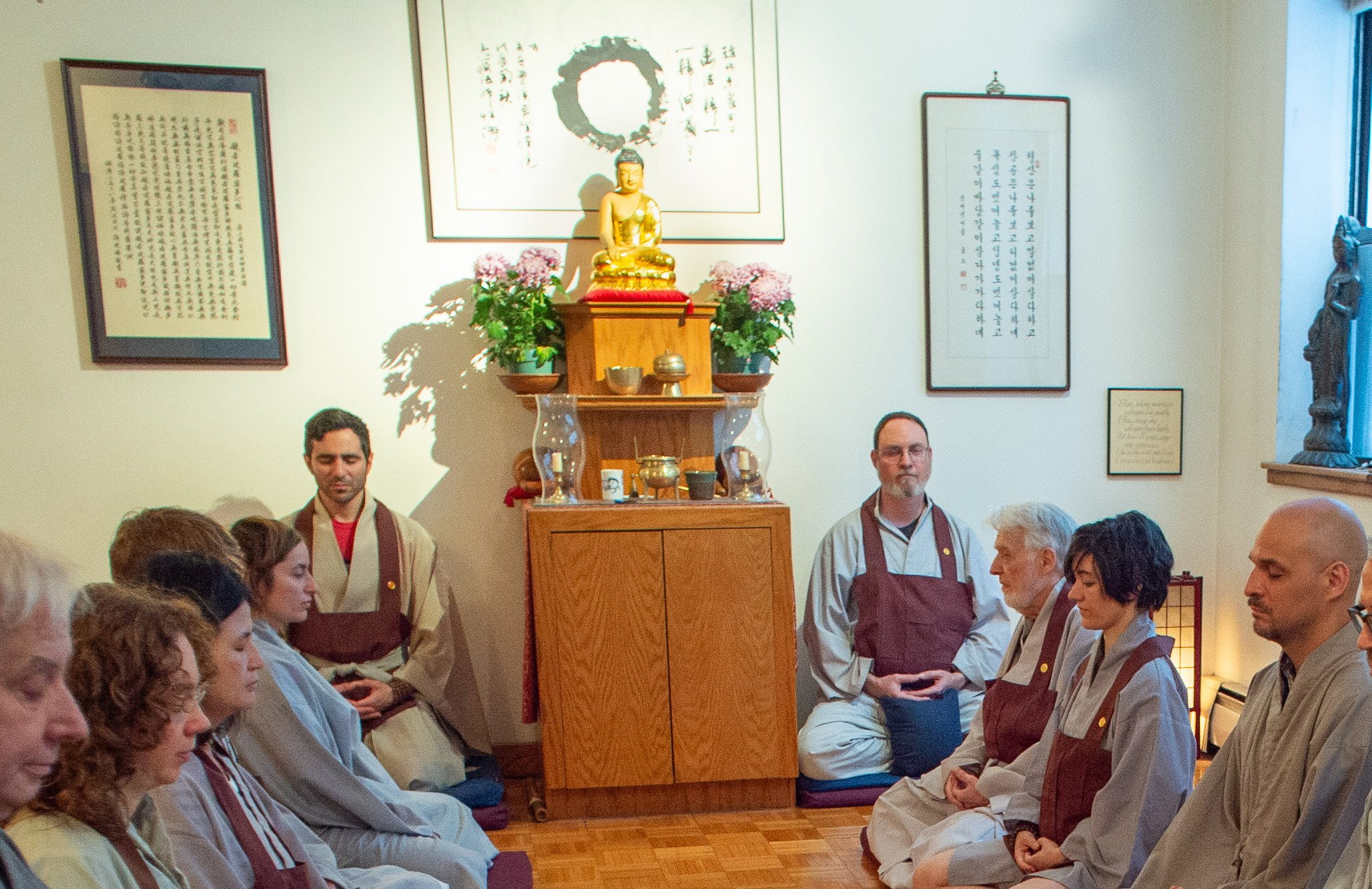 The Buddha altar at Chogye International Zen Center, 400 East 14th Street, 2016. Golden Buddha statue with fresh flowers, flanked by calligraphy and an ensō painting.