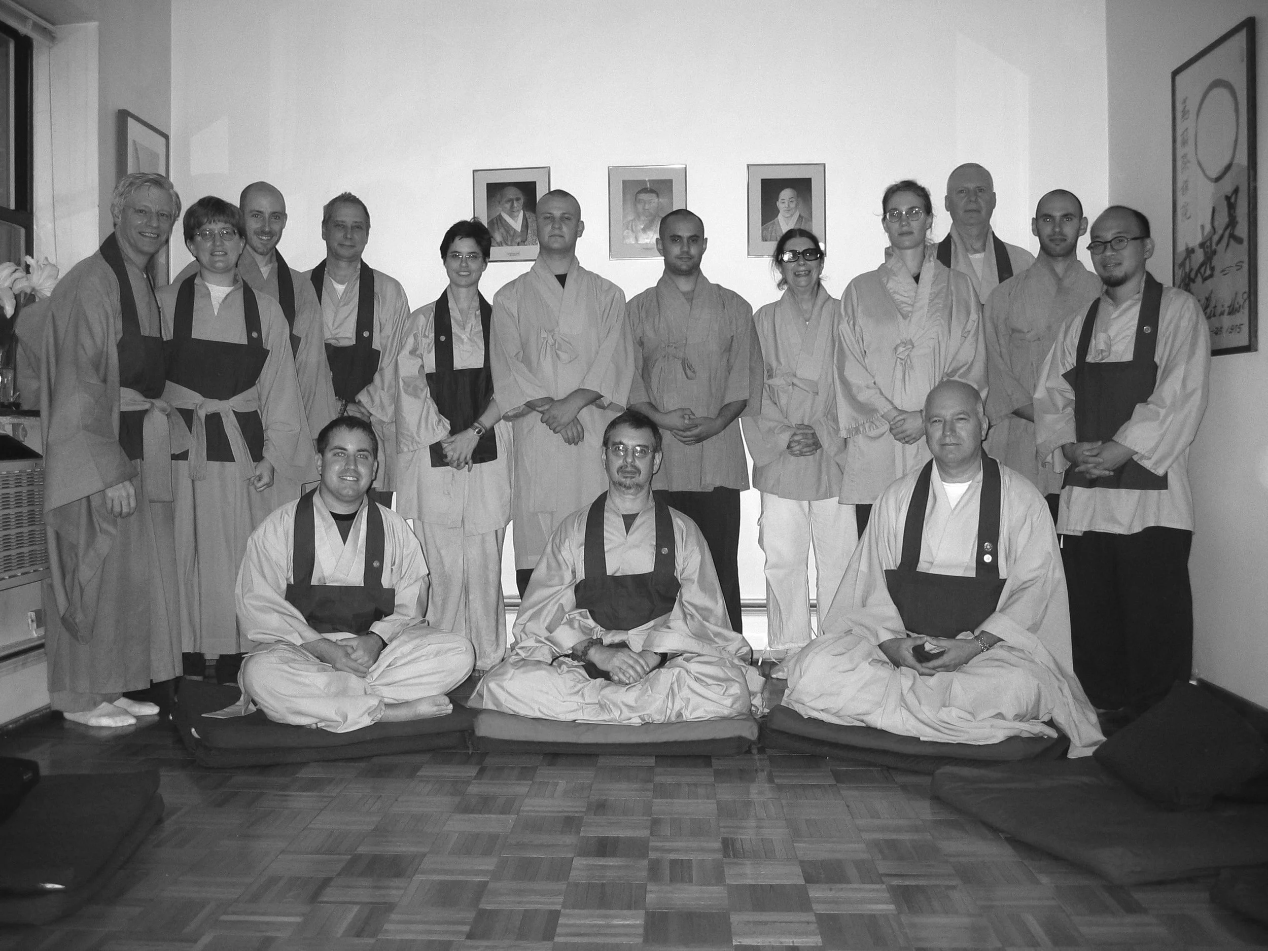 Retreat group photo, Chogye Zen Center, 400 East 14th Street, 2004. Zen Master Wu Kwang seated center front. Practitioners in Korean Zen robes. Framed portraits and ensō painting visible on the walls.