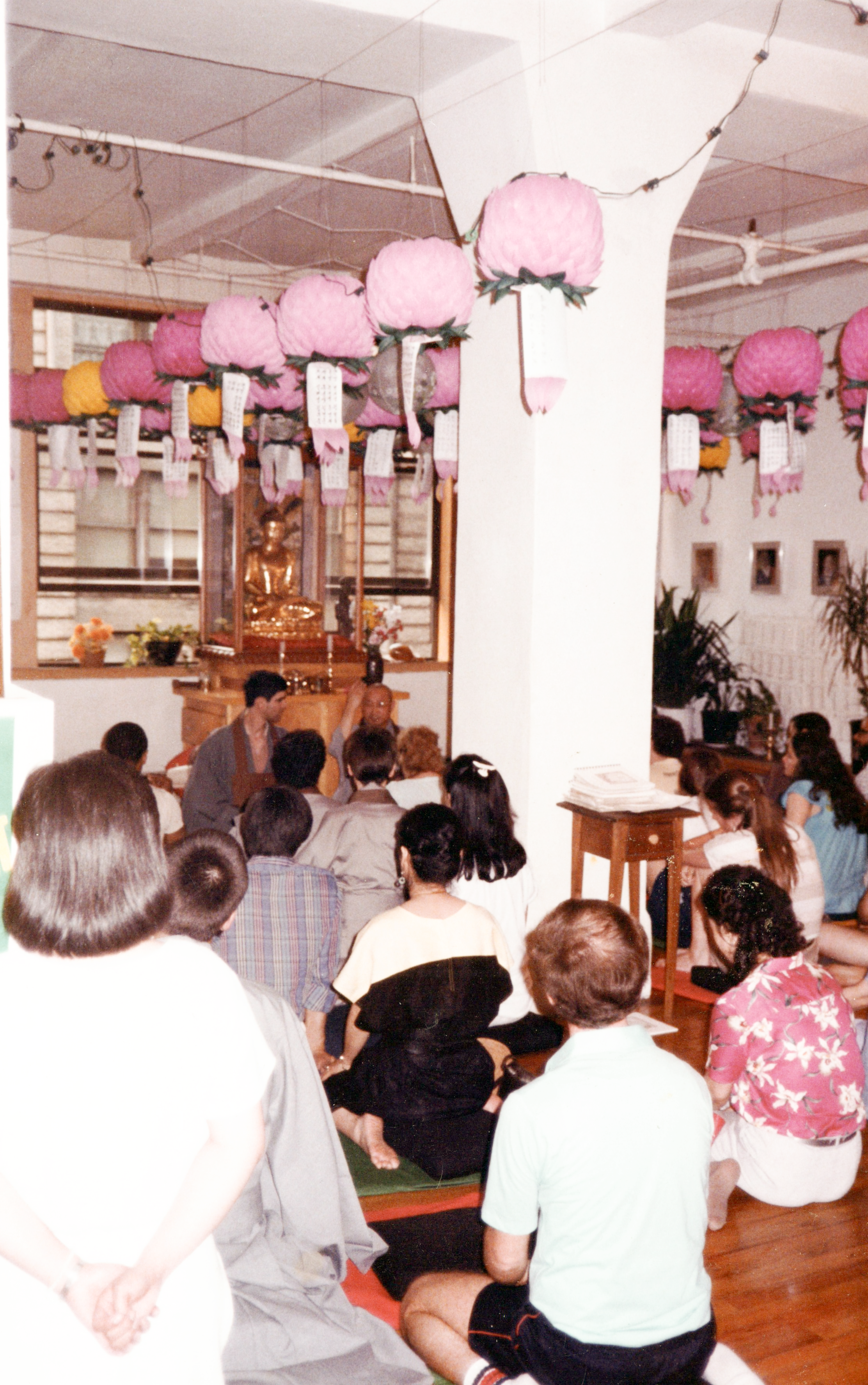 Dharma talk at 42 West 17th Street, circa 1980s. Two teachers seated at the altar, with practitioners facing them. The room is decorated with colorful lotus lanterns for Buddha's Birthday.