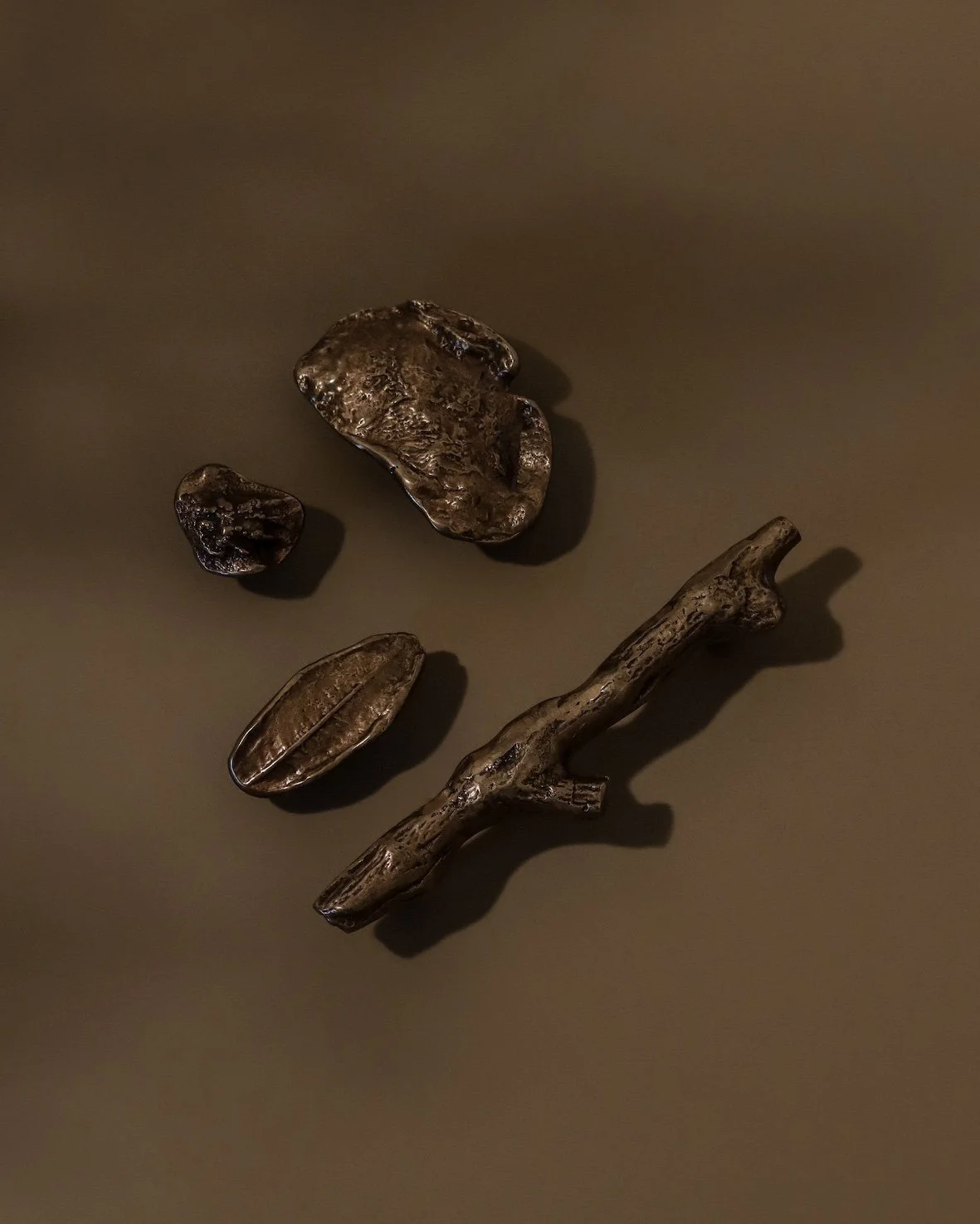 Collection of bronze objects including a stick, leaf, and stones on a brown surface