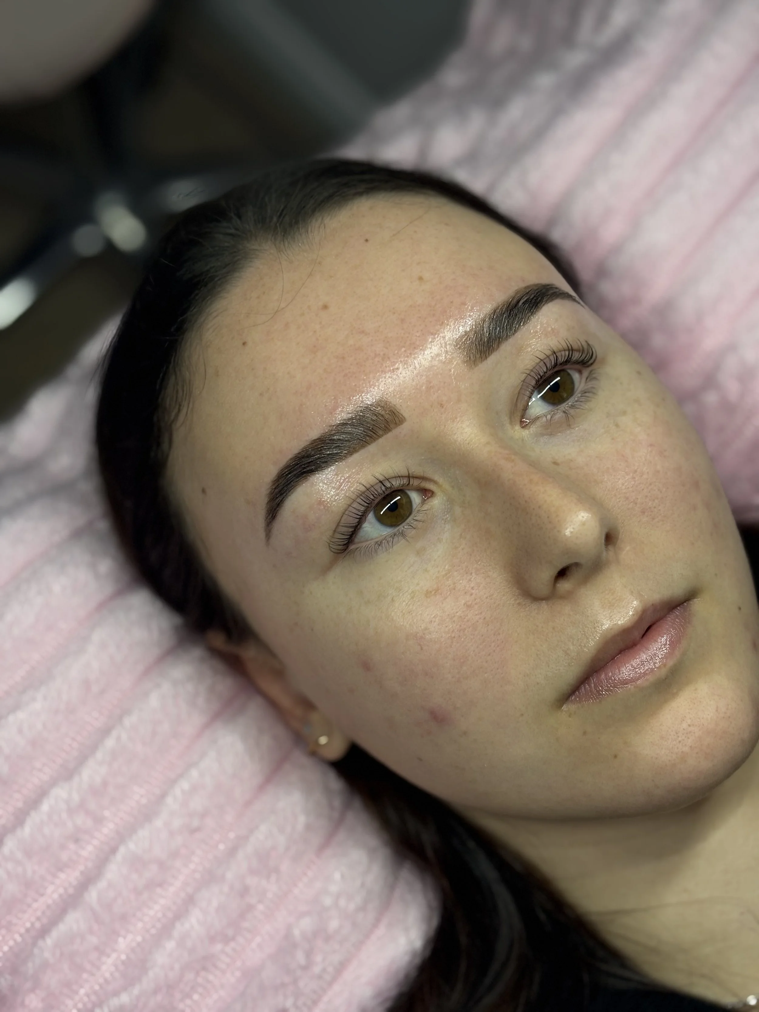 Close-up of a woman's face showing her eyebrows and eyes, with her lying on a pink soft surface.
