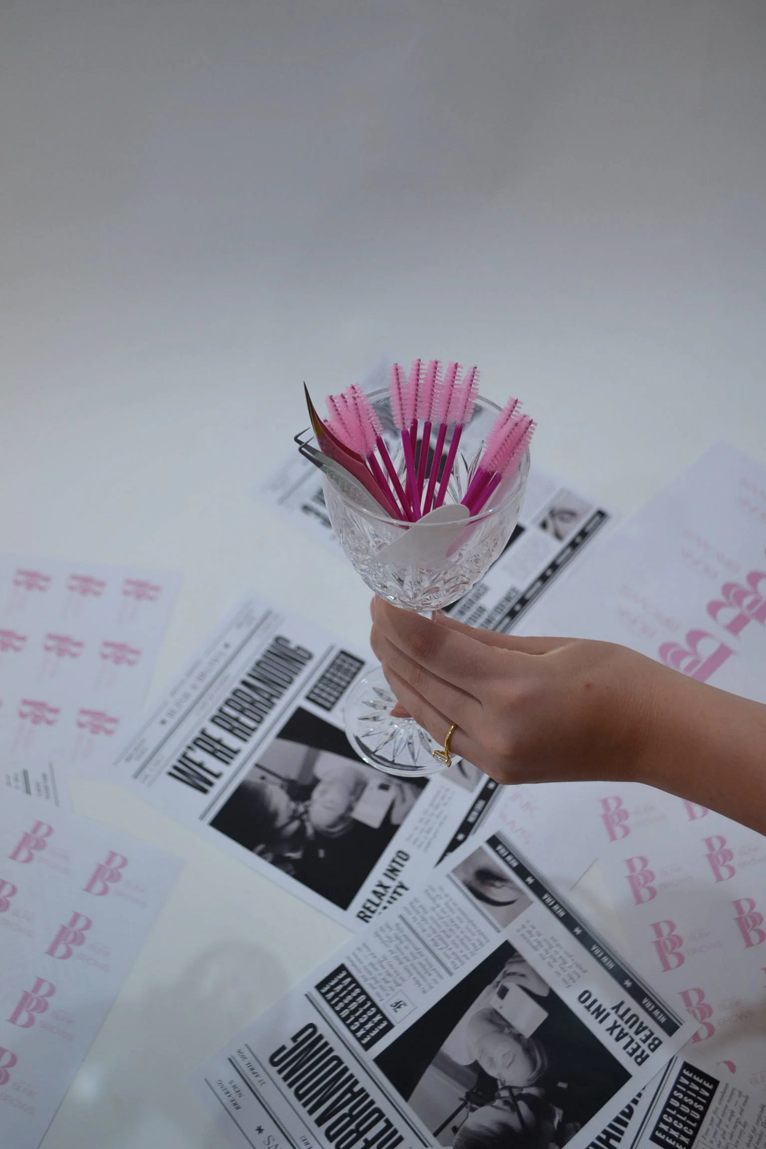 A person holding a glass bowl with several pink cleaning brushes inside, placed on a table covered with newspapers.