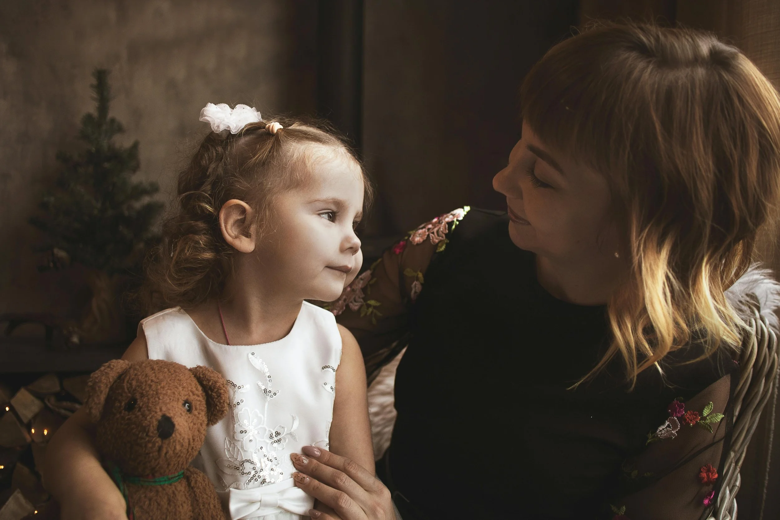A woman embraces a little girl holding a teddy bear, representing childhood and emotional support in parts work, shared by Inside Retreats.
