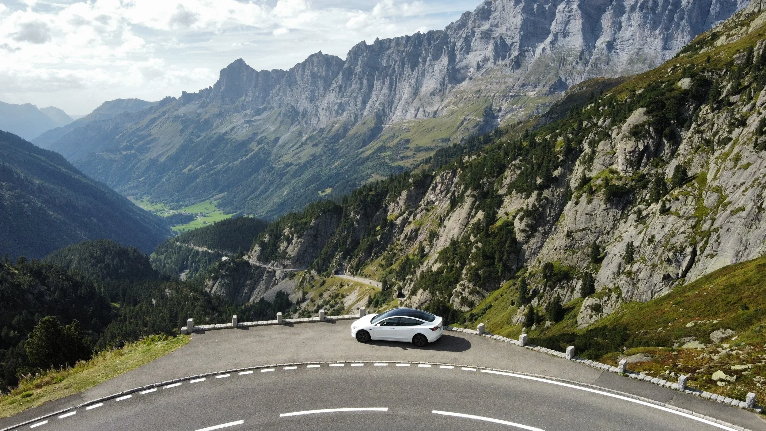 White Tesla on a mountain road in the Swiss Alps, aerial view