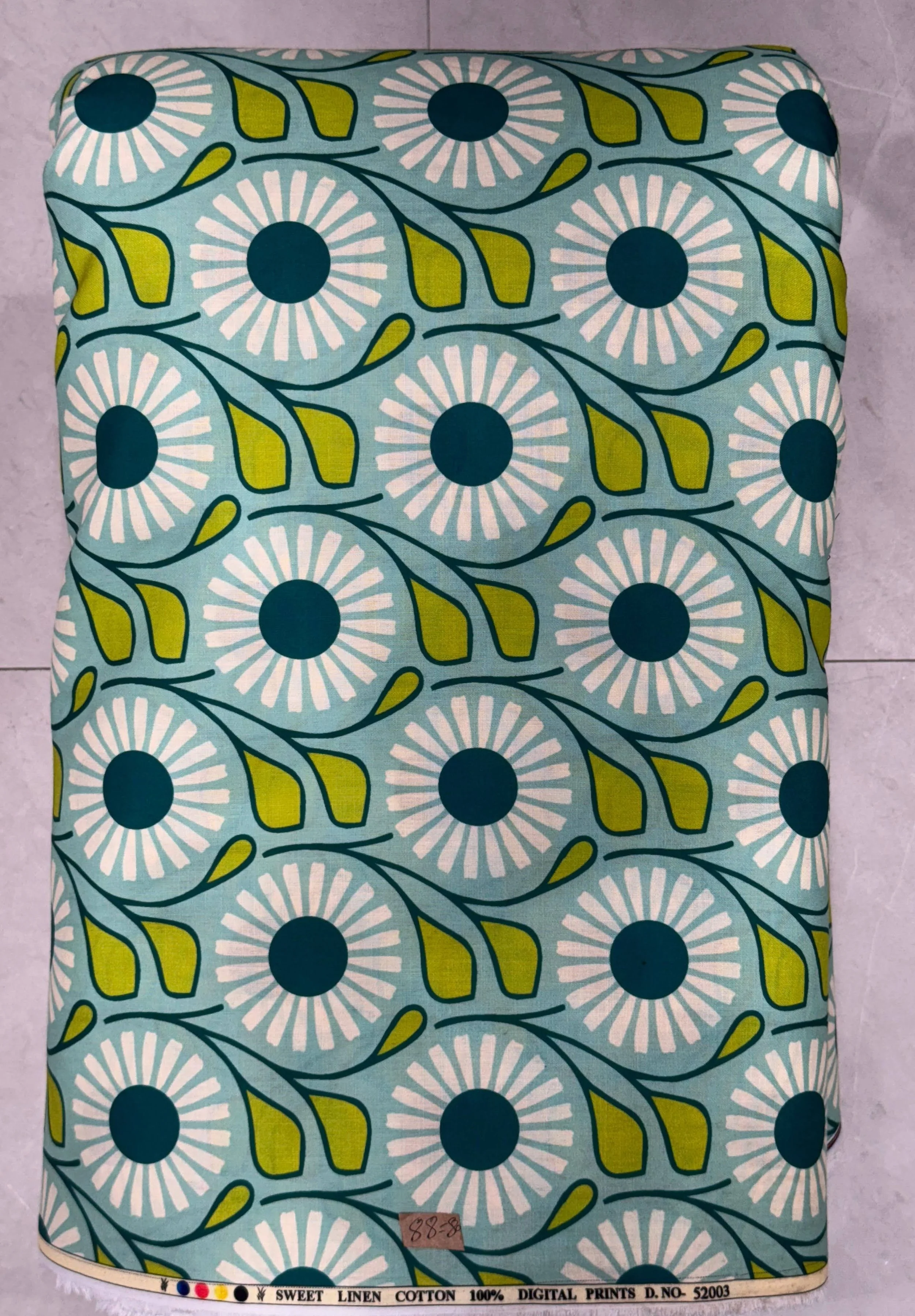 Textured turquoise-green fabric featuring a repeating retro geometric floral print with bold circular medallion patterns, detailed with subtle linear accents for contemporary apparel collections.