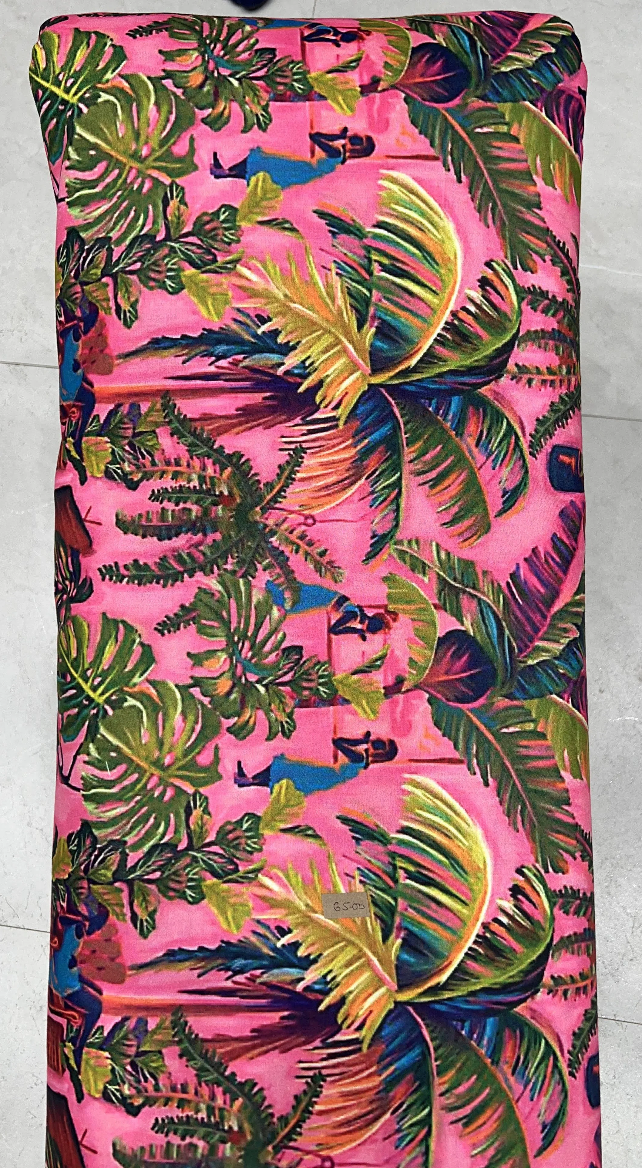 Vibrant pink fabric featuring a tropical print with lush green palm fronds, detailed botanical foliage, and colorful exotic birds.