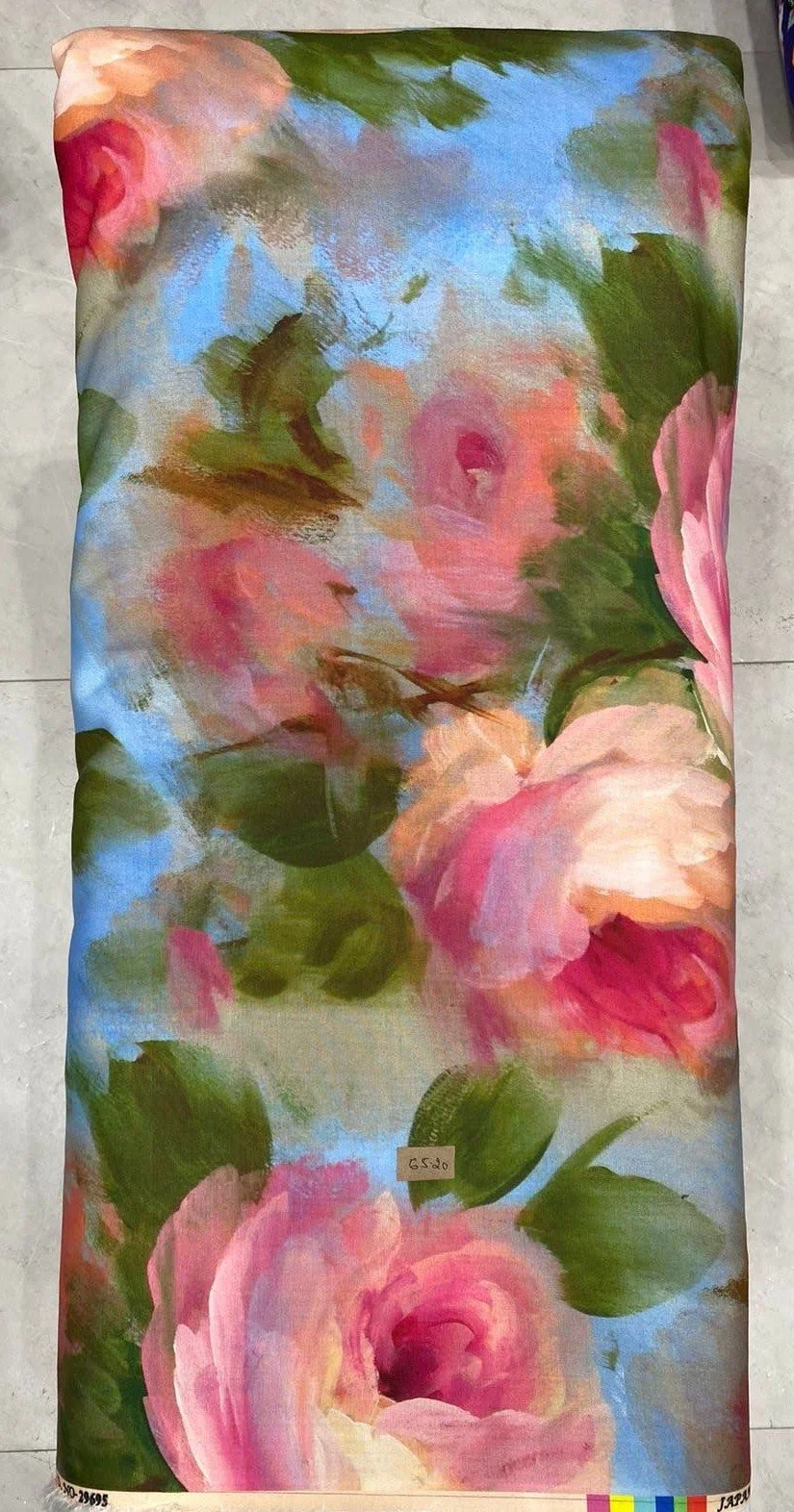 Soft, airy pastel fabric featuring a gentle watercolor floral print with soft pink roses, delicate green leaves, and muted blue and grey accents against a light background.