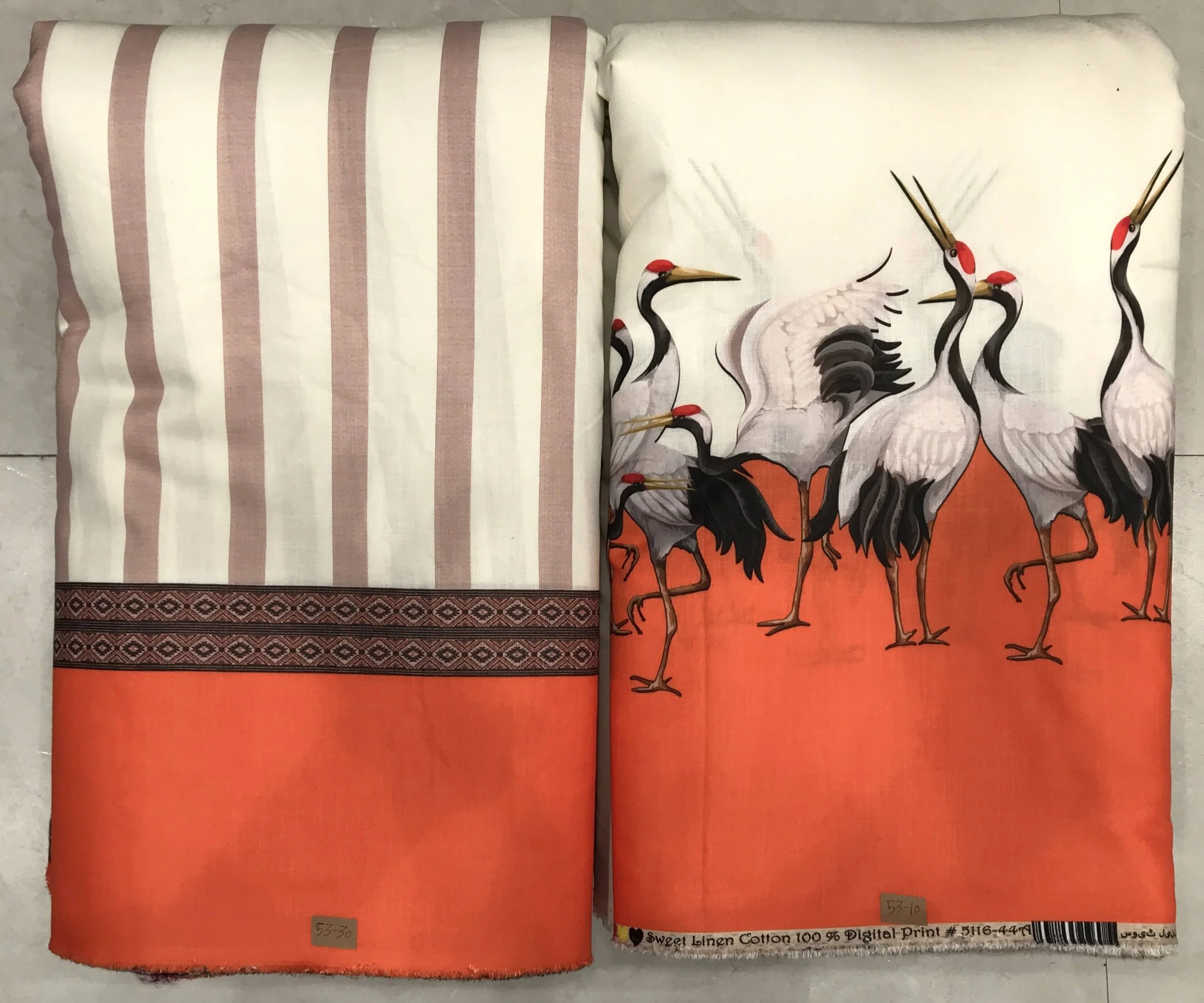 Rich burnt-orange and deep charcoal fabric featuring a striking panel composition with vertical striped panels on the left and an illustrative wildlife motif featuring graceful standing cranes along the right border.