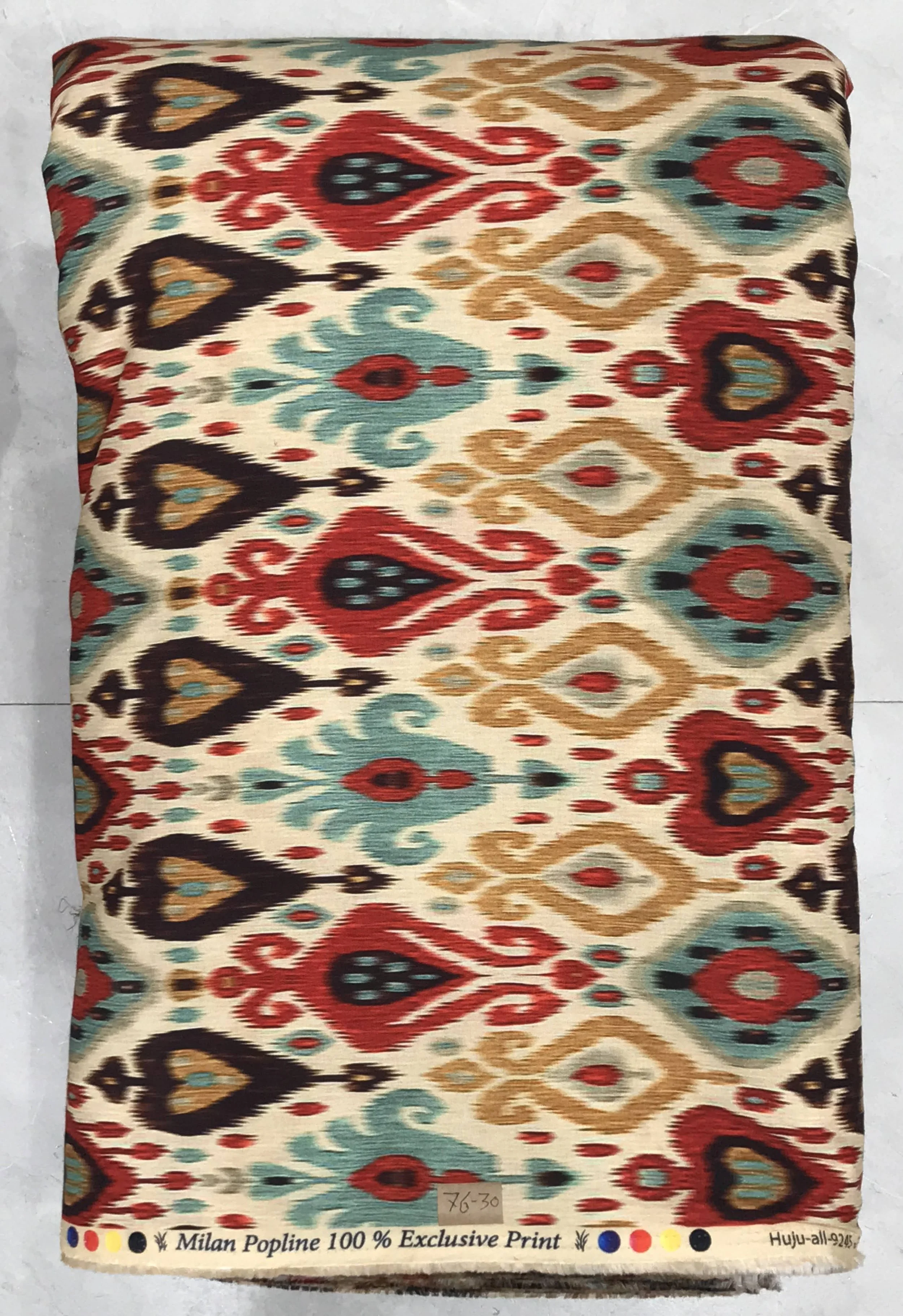 Textured cream and beige background featuring an intricate multicolored tribal ikat geometric print with symmetrical diamond motifs, ornate borders, and accents of burgundy, deep green, and golden yellow.