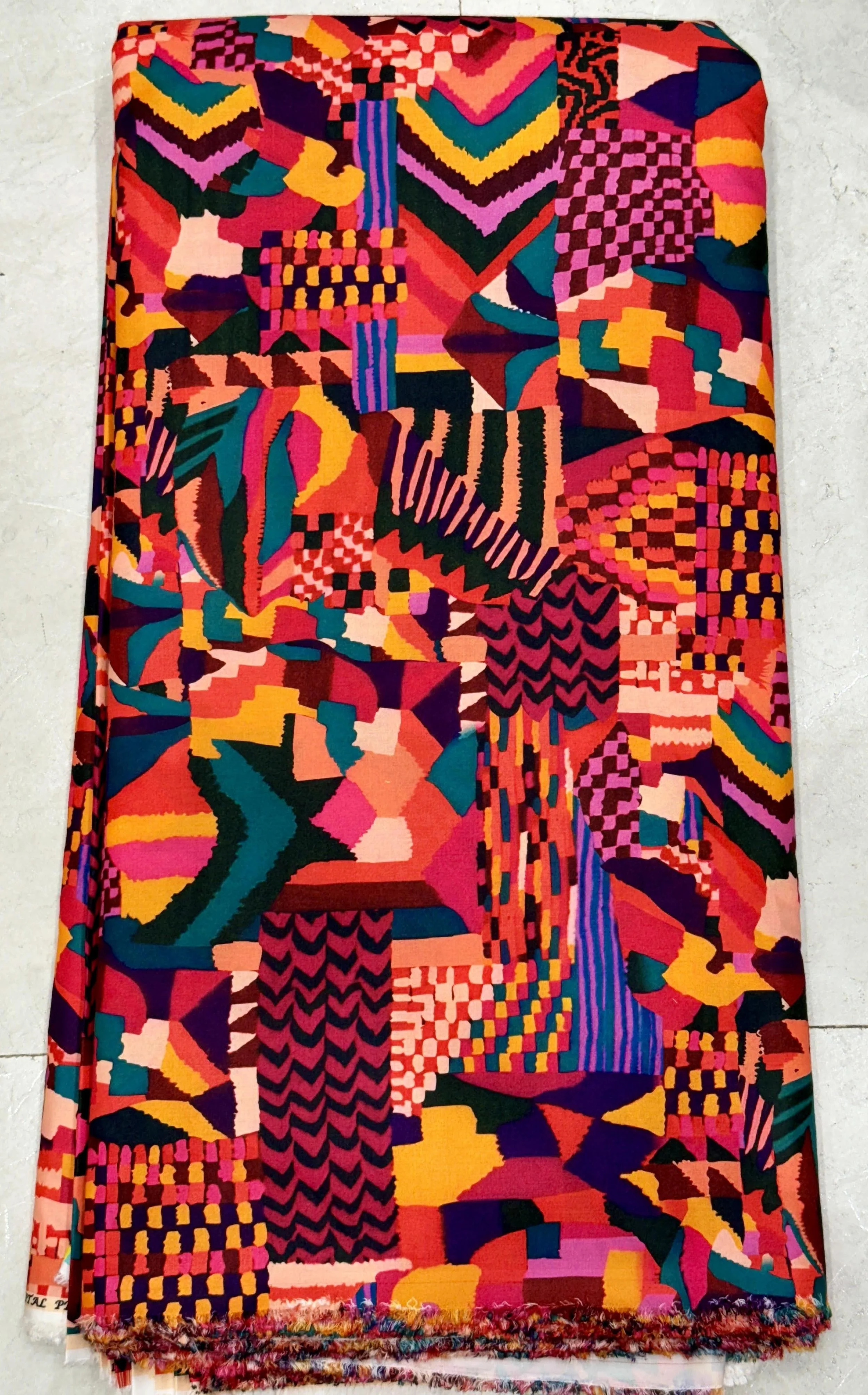 Vibrant multi-colored fabric featuring an energetic abstract mosaic design with bold geometric blocks in rich red, orange, blue, green, and purple tones.