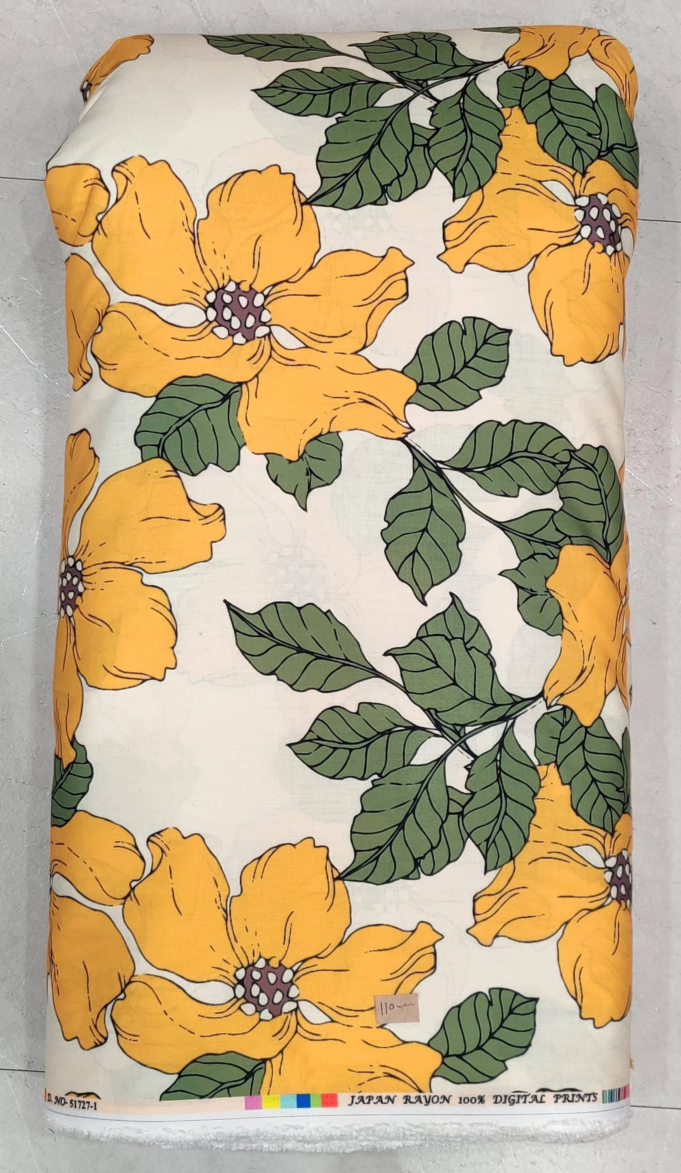 Soft cream-toned fabric displaying a scattered pattern of vibrant golden-yellow blossoms, dark olive-green leaves, and slender stems.