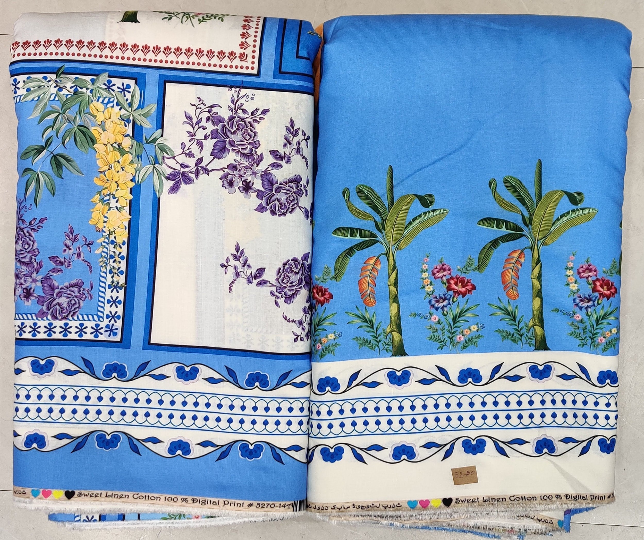 Vibrant sky-blue fabric featuring a scenic tropical island print with stylized palm trees, exotic birds, and a decorative geometric border along the lower edge.