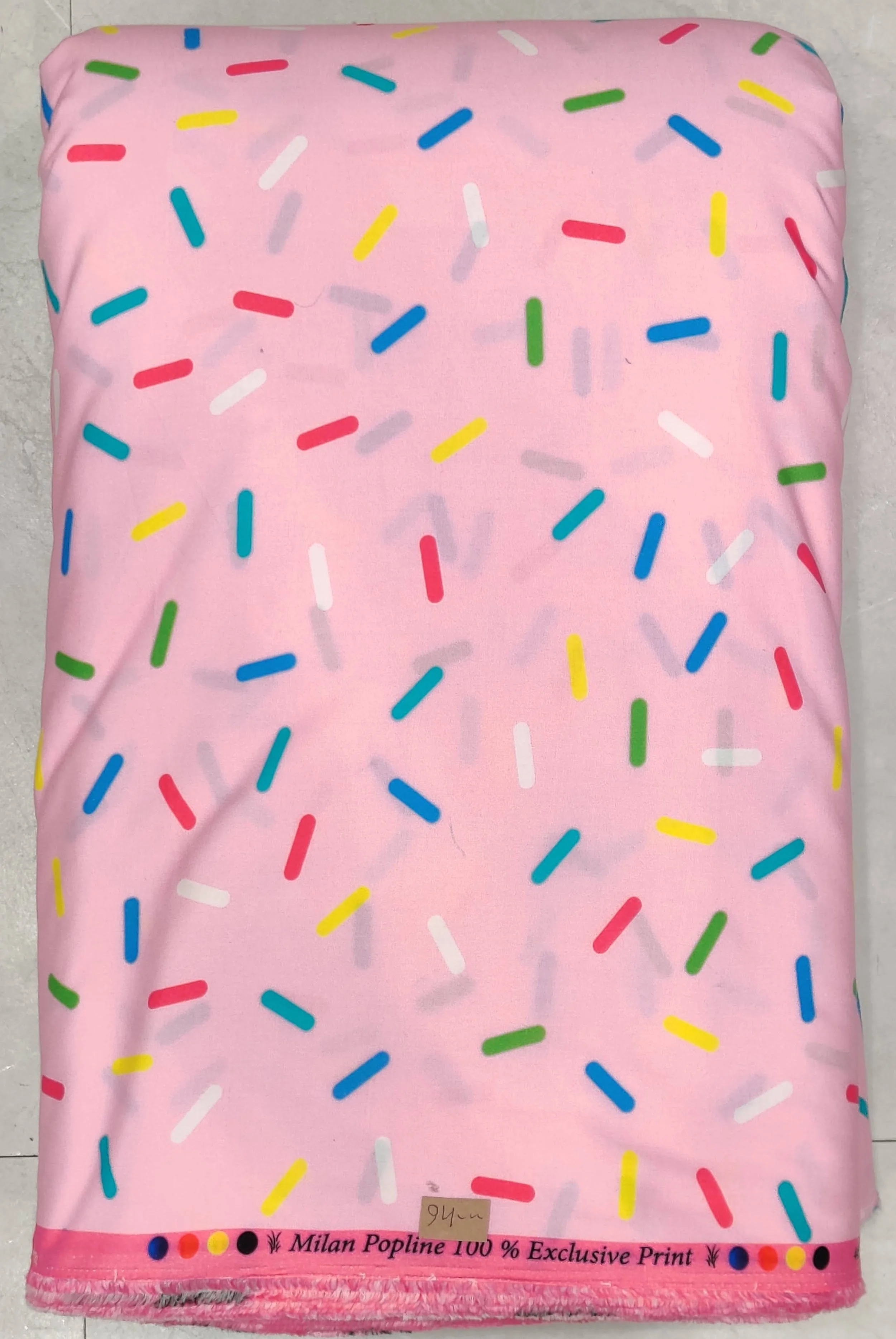 Soft pastel-pink background featuring a playful, whimsical confection print with a scattering of colorful, multi-shaped sugar sprinkles in shades of blue, yellow, purple, and green.