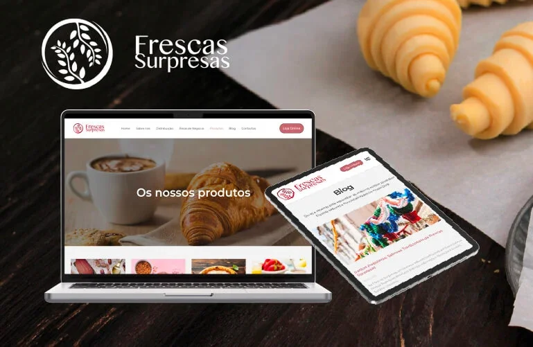 Imagem de um laptop e um tablet exibindo o site de uma loja chamada 'Frescas Surpresas', com foco em produtos alimentícios, especialmente croissants e bebidas quentes, sobre uma mesa de madeira