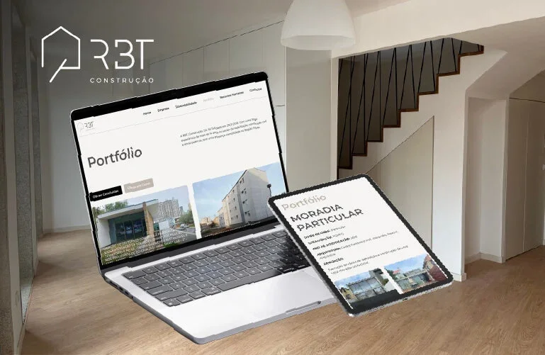 Imagem de um laptop e uma tablet exibindo um portfólio de construção da empresa ARBT, sobre uma superfície de madeira, dentro de uma sala com escada de madeira ao fundo.