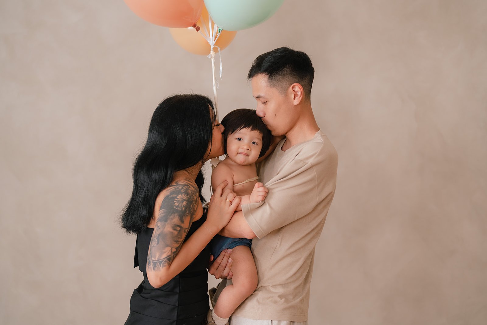 A family of three celebrates with balloons, with the father holding a young child, the mother kissing the child's cheek.