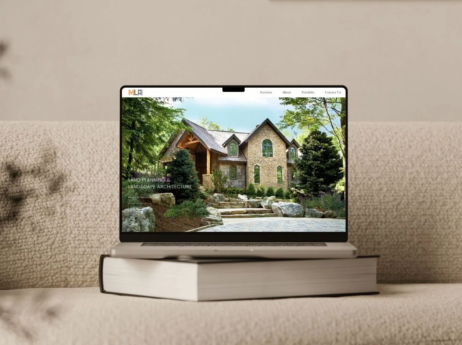 Laptop on a book displaying a home design website with a large house and landscaping.