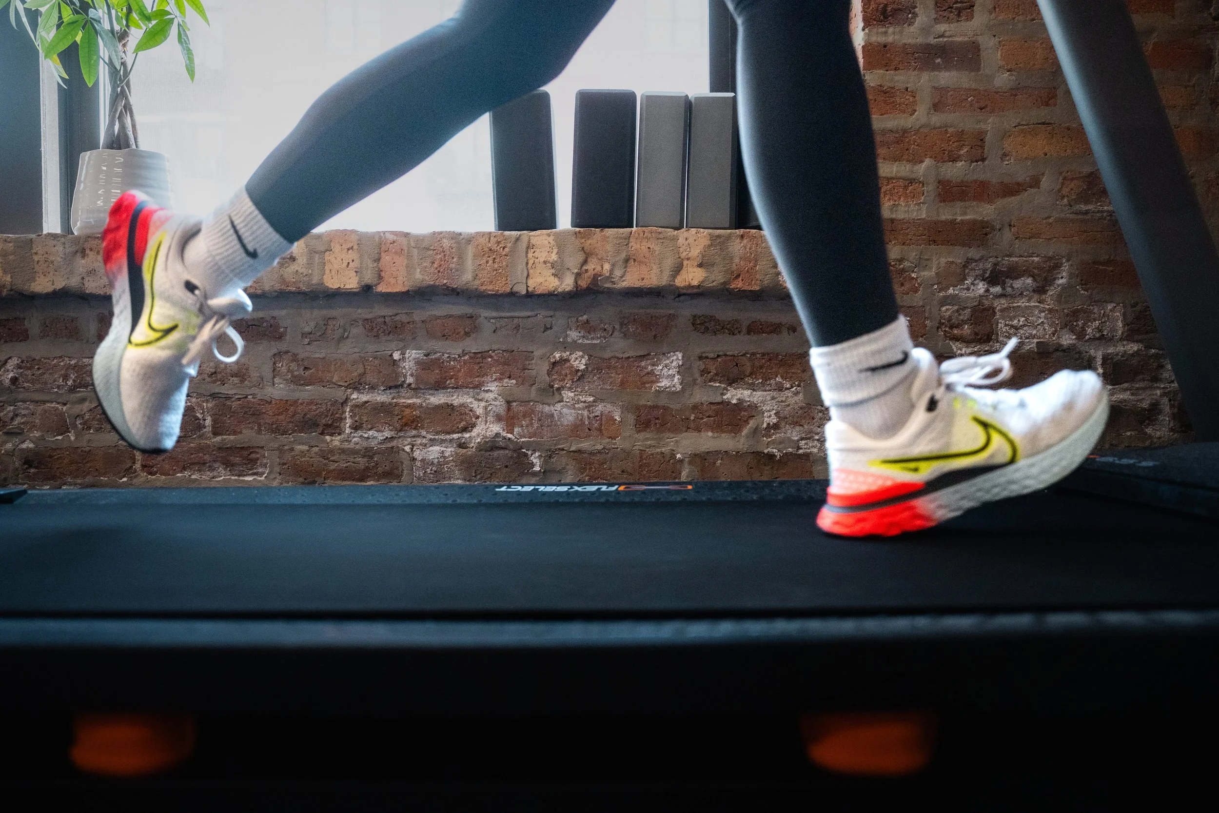 Knee down view of legs running on a treadmill wearing leggings, socks, and nike sneakers.