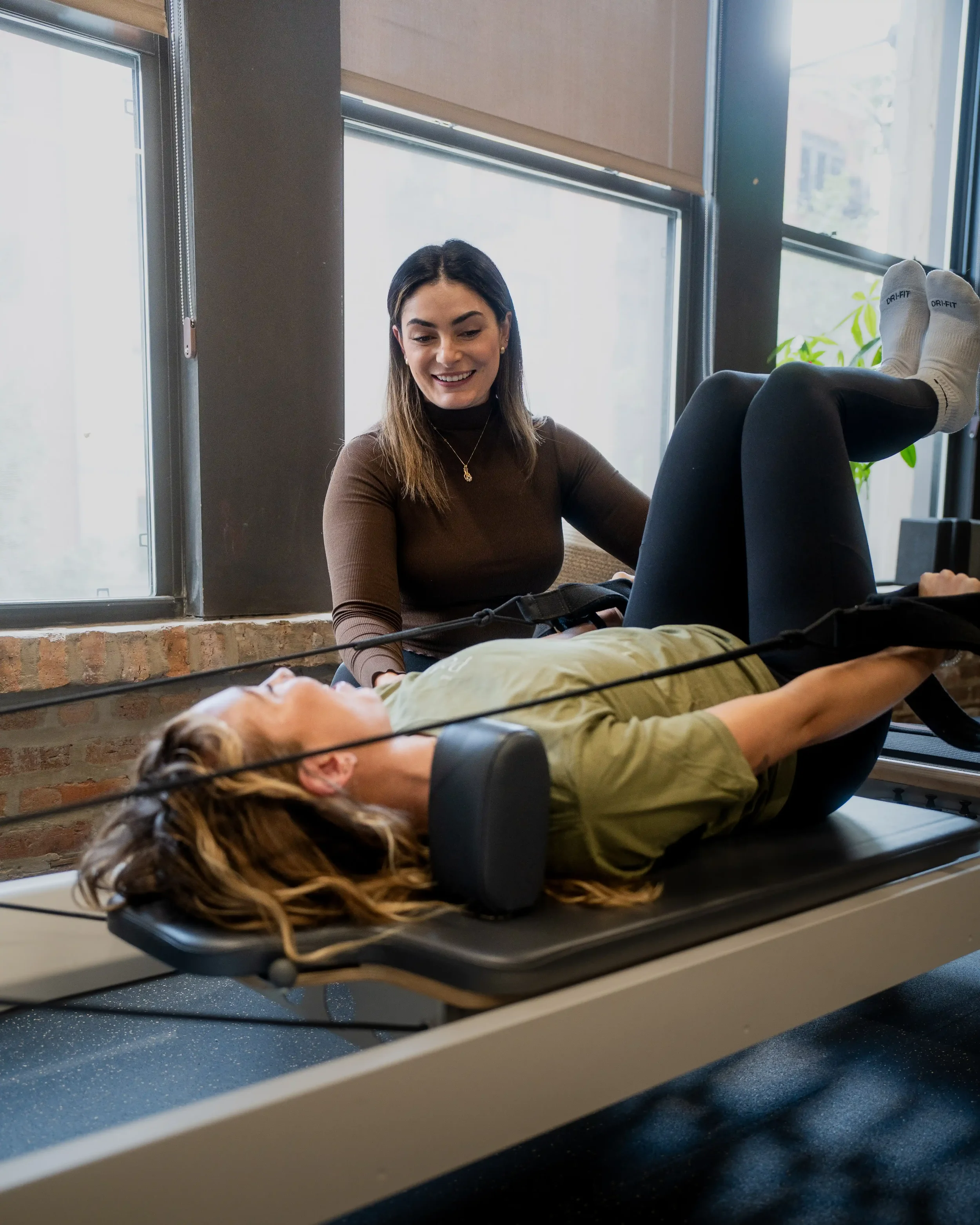 Woman on a reformer doing a private training session with coaching from a physical therapist.
